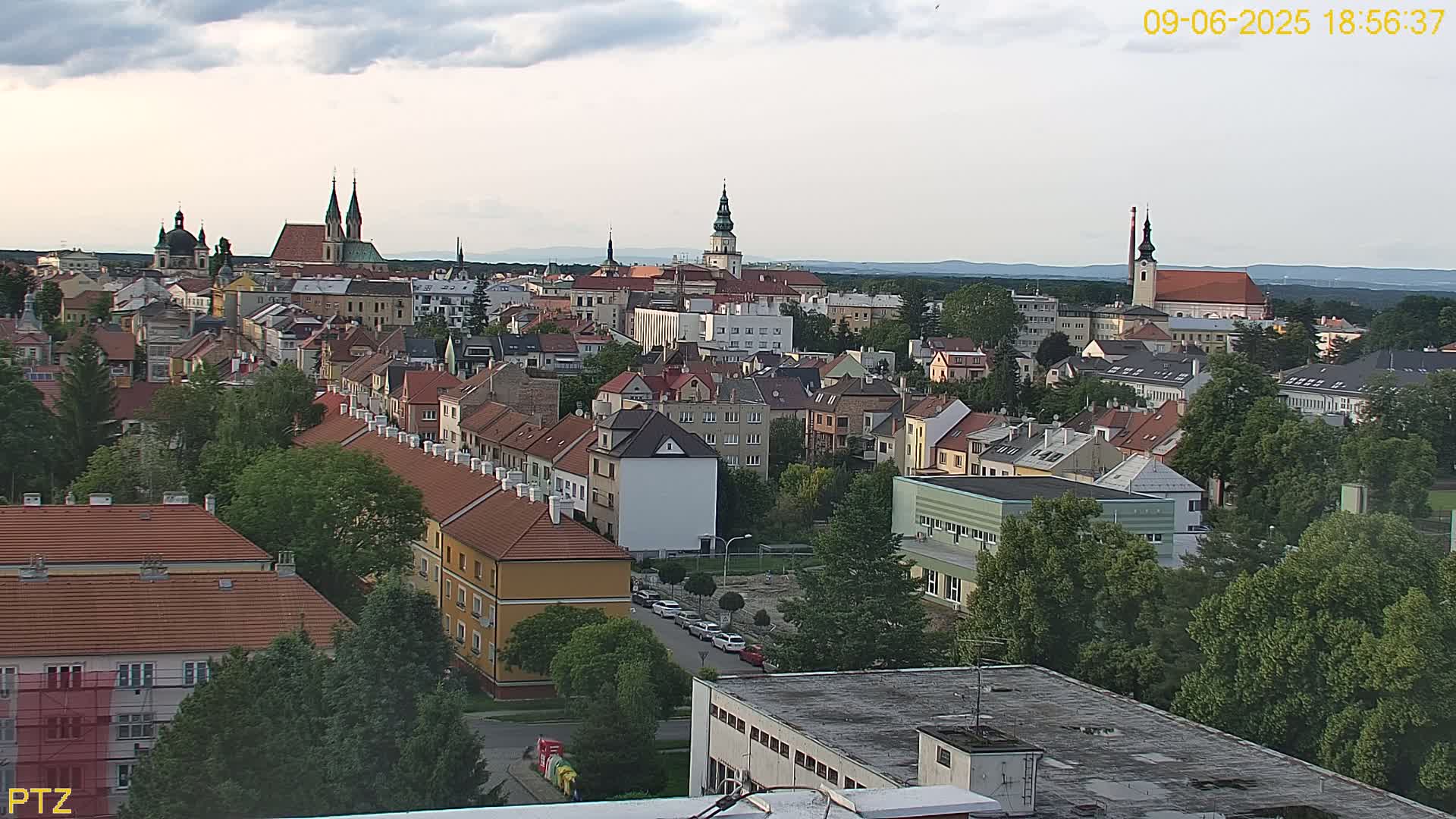 An elevated view of a European town on a partly cloudy evening, showing many buildings with red-tiled roofs and several churches interspersed among the residences.