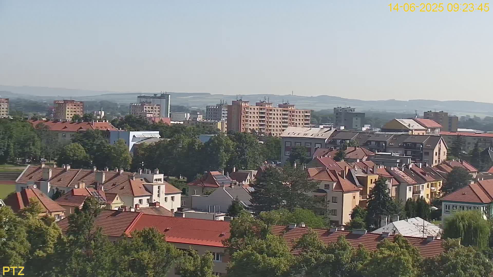 A sprawling town with mostly red-tiled roofs and several multi-story buildings is visible under a clear, sunny sky.