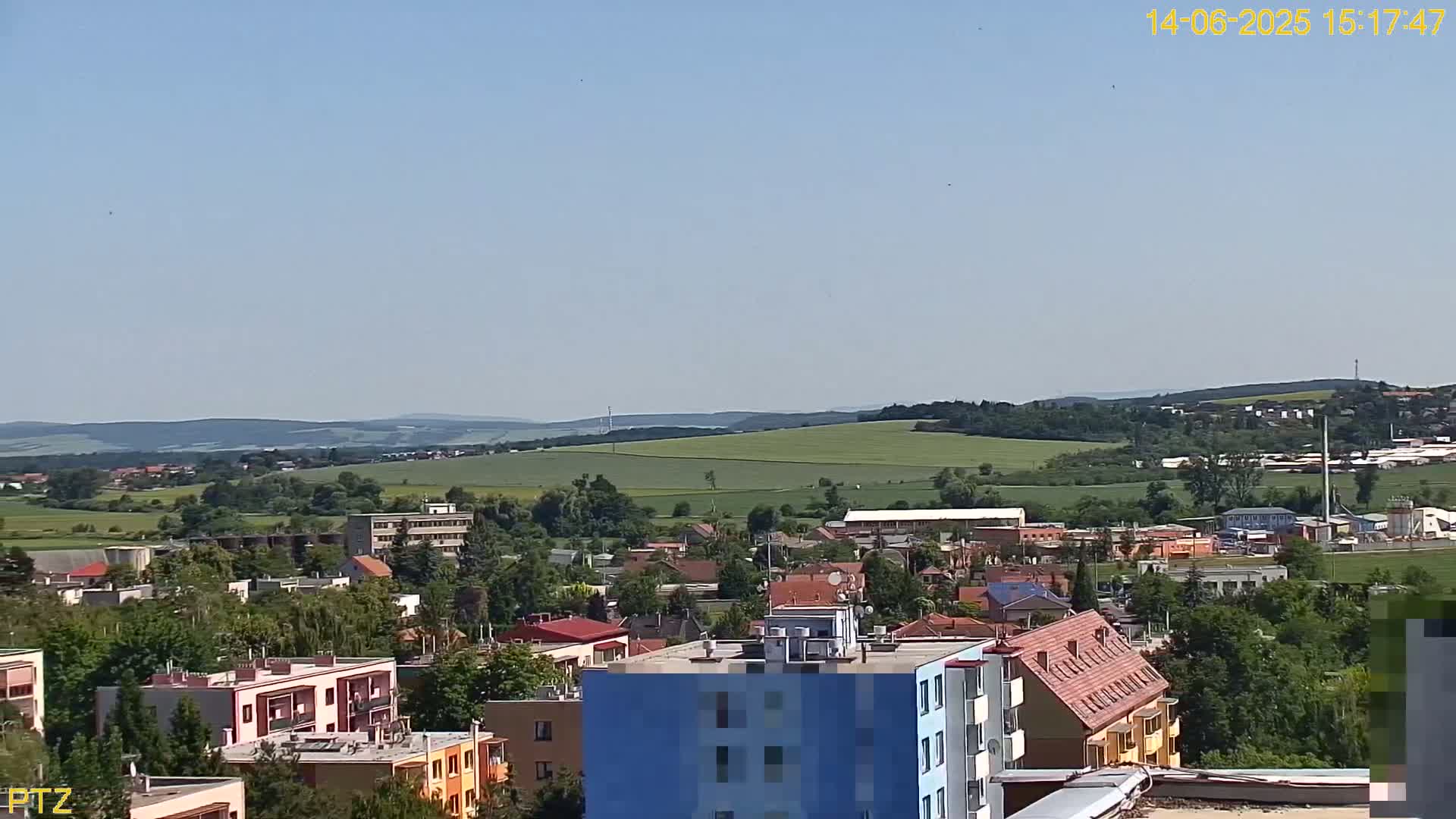 A clear, sunny day reveals a sprawling town nestled amongst rolling green hills and fields.