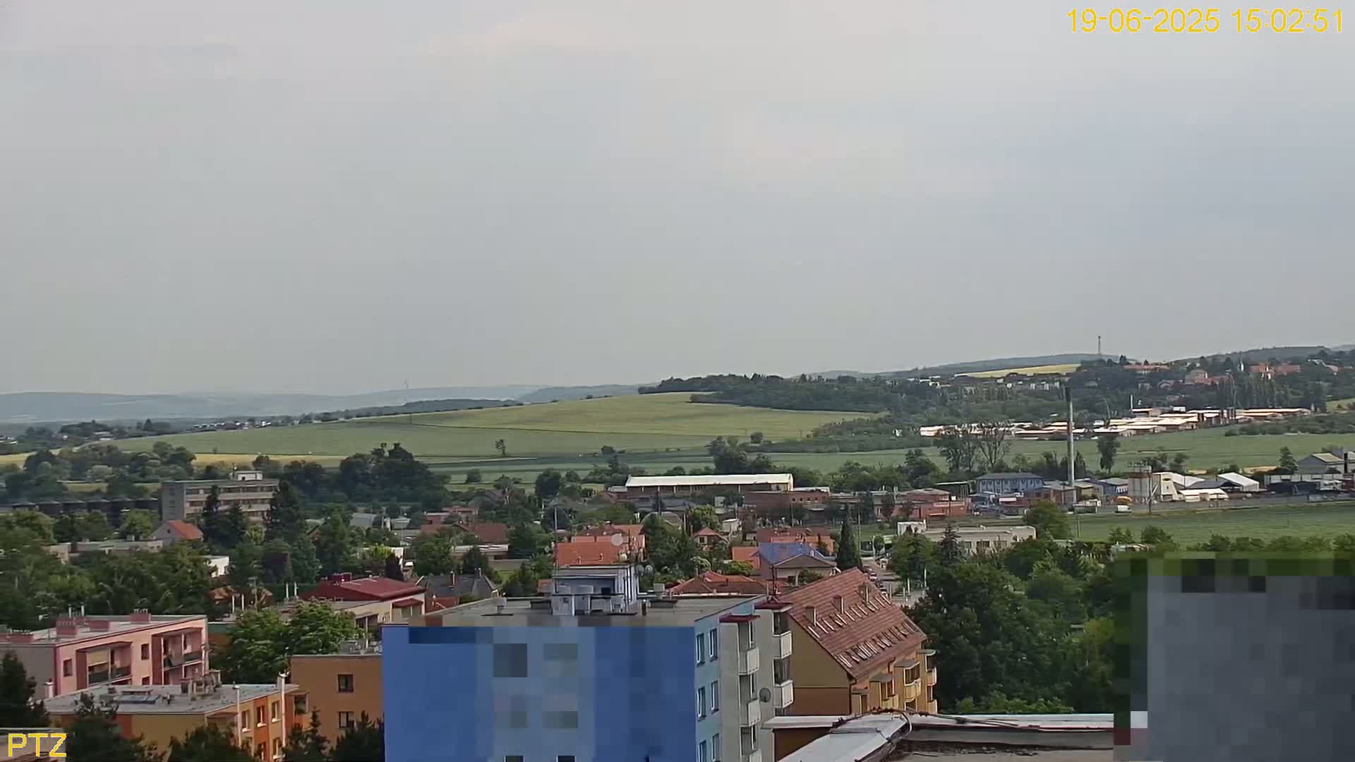 A hazy, overcast day reveals a sprawling town nestled beside rolling green hills and fields, with numerous buildings and trees visible.