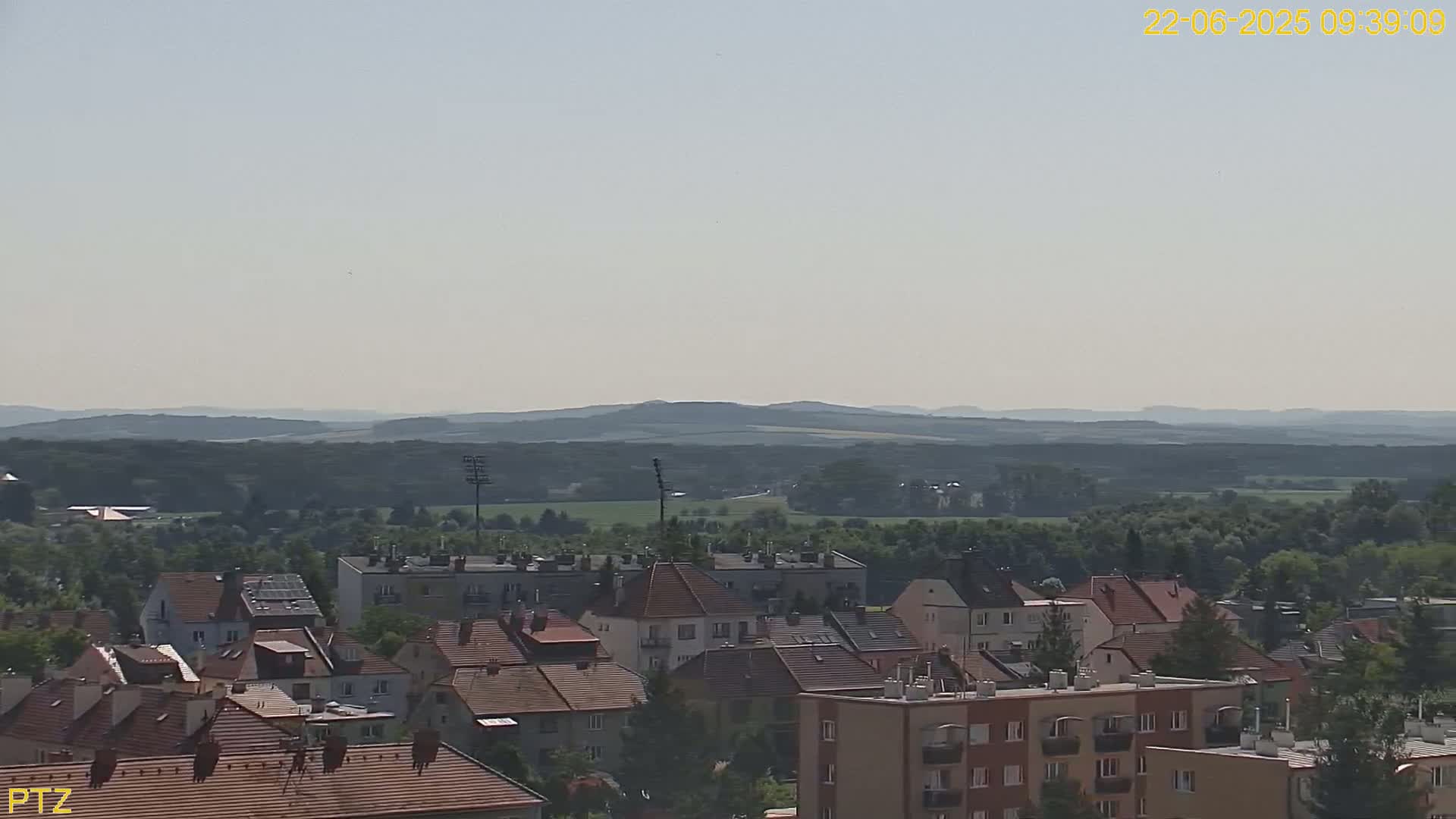 A hazy, sunny day reveals a view of a town nestled amongst green hills and trees.