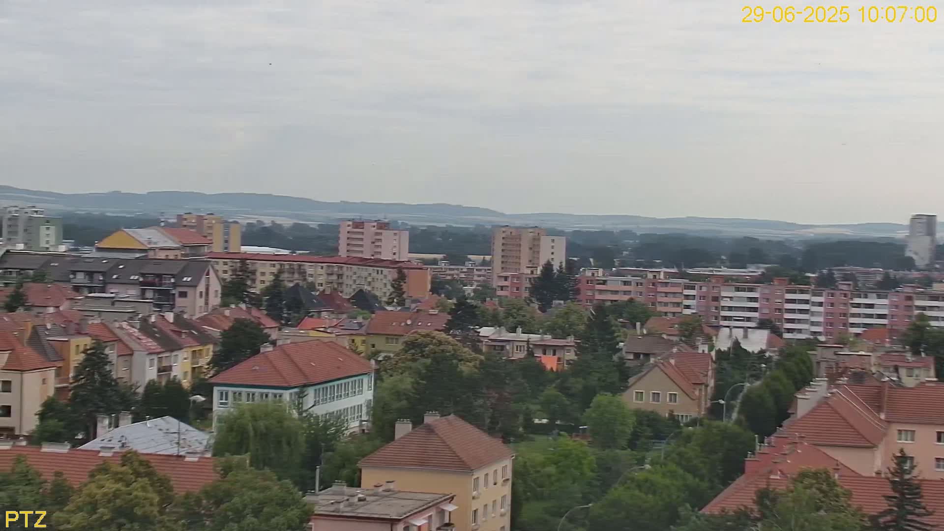 An overcast day reveals a dense residential area with multi-story buildings and a mix of house styles, set against a backdrop of distant hills.