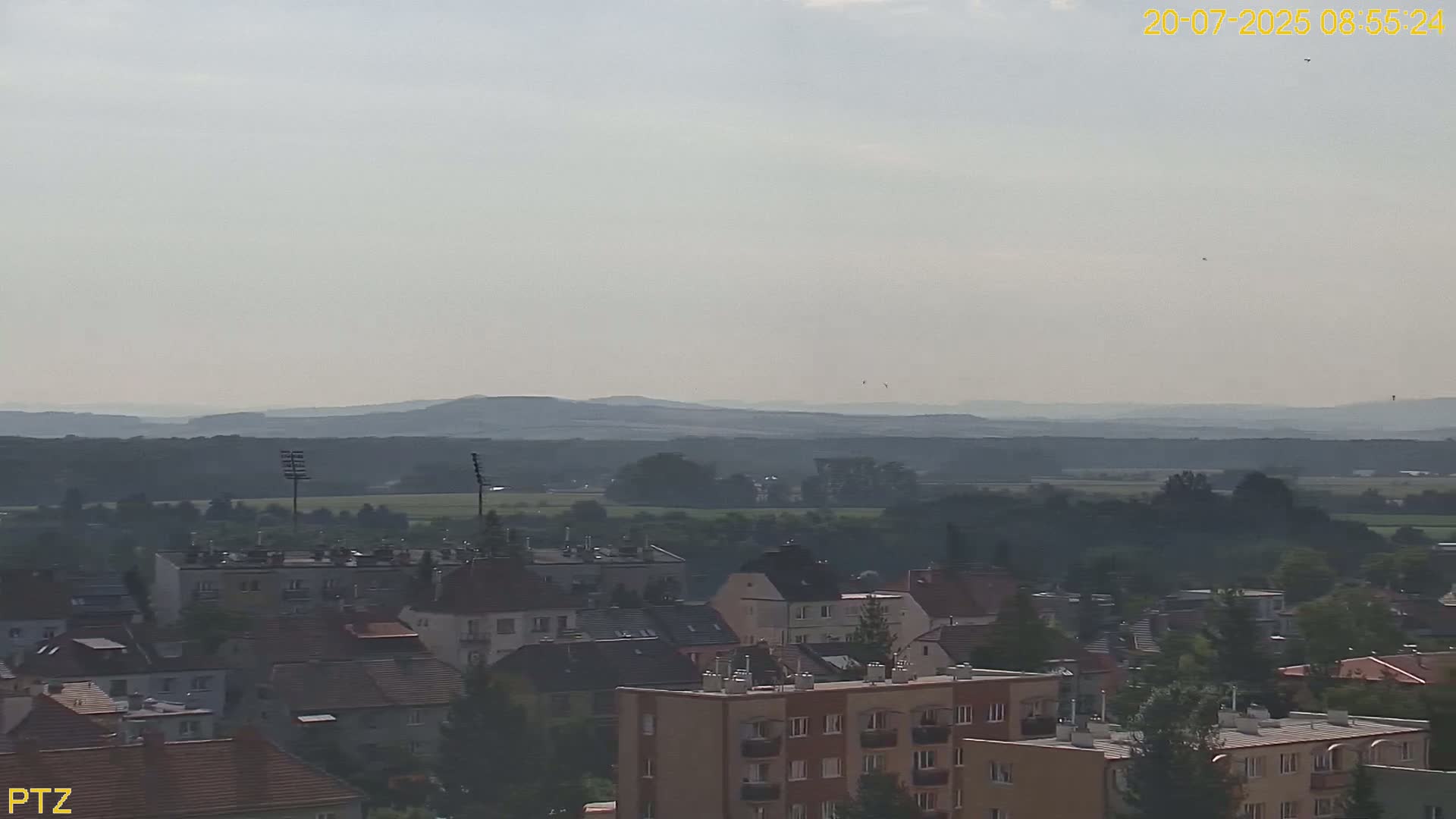A hazy view shows a town of low-rise buildings stretching to distant, low mountains under a light, overcast sky.