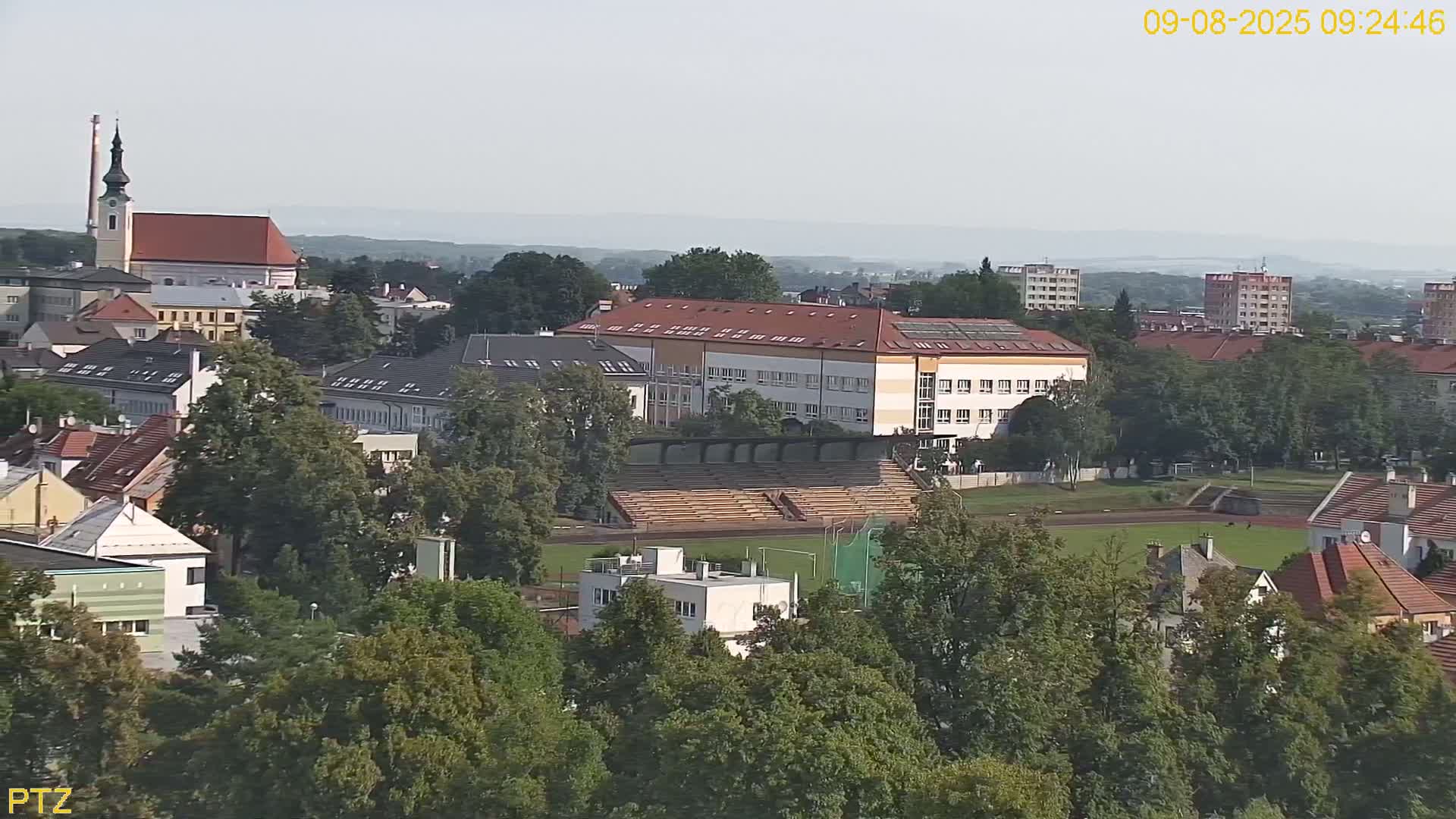 An elevated view shows a town on a hazy day, with a school, stadium, and church visible amongst the buildings and trees.