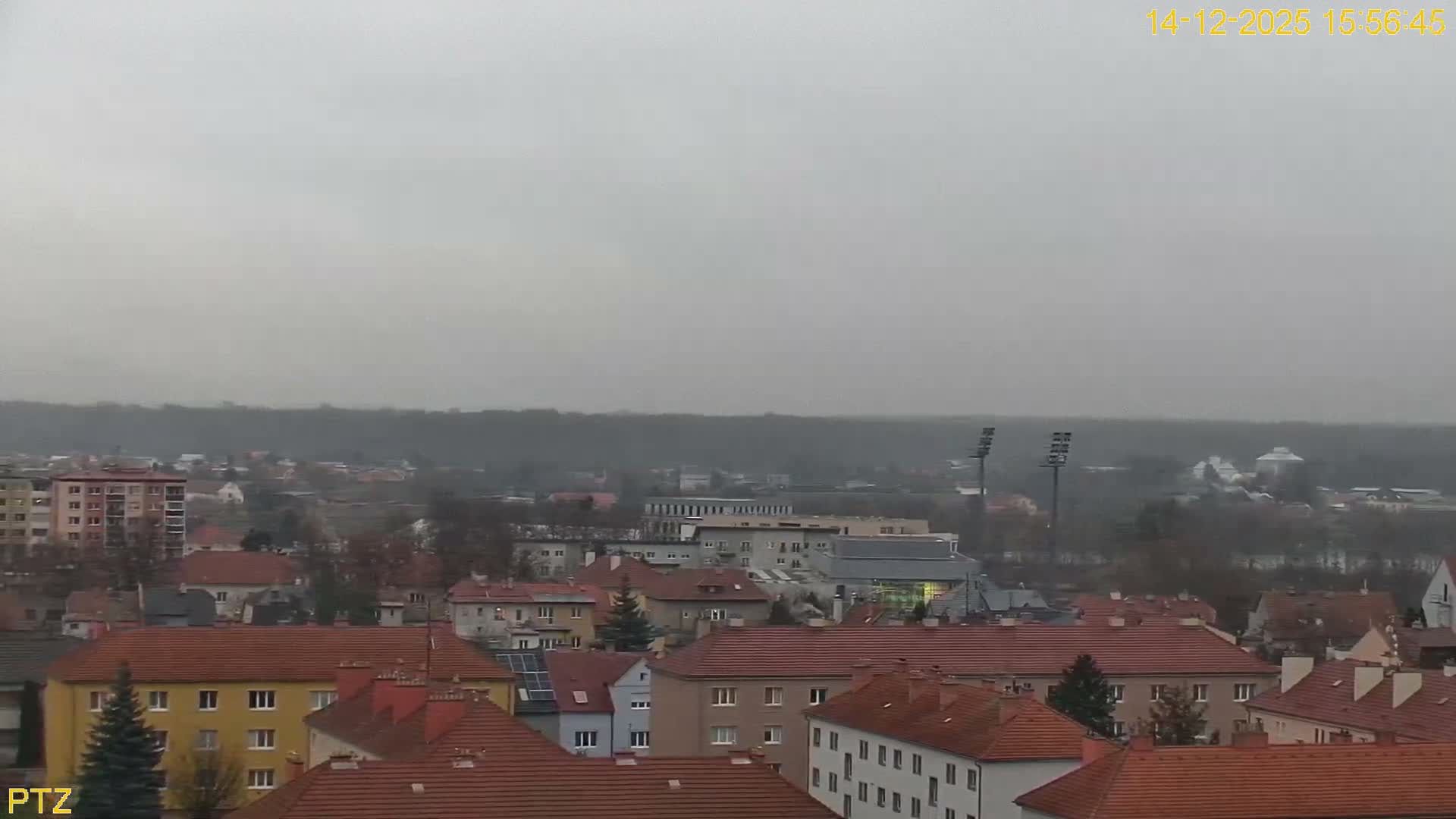 An elevated view reveals a dense urban landscape with a mix of multi-story buildings and houses with pitched roofs, all under a dull, heavily overcast, and hazy sky.