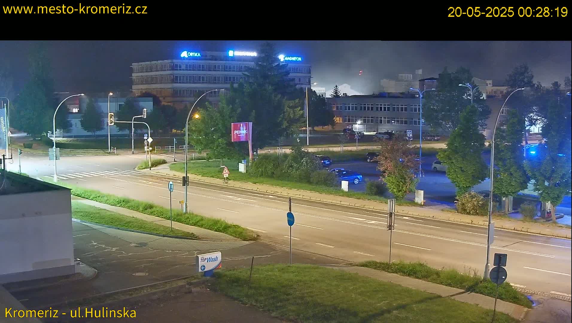 A nighttime view of a multi-lane road with several cars parked in a lot next to industrial buildings.