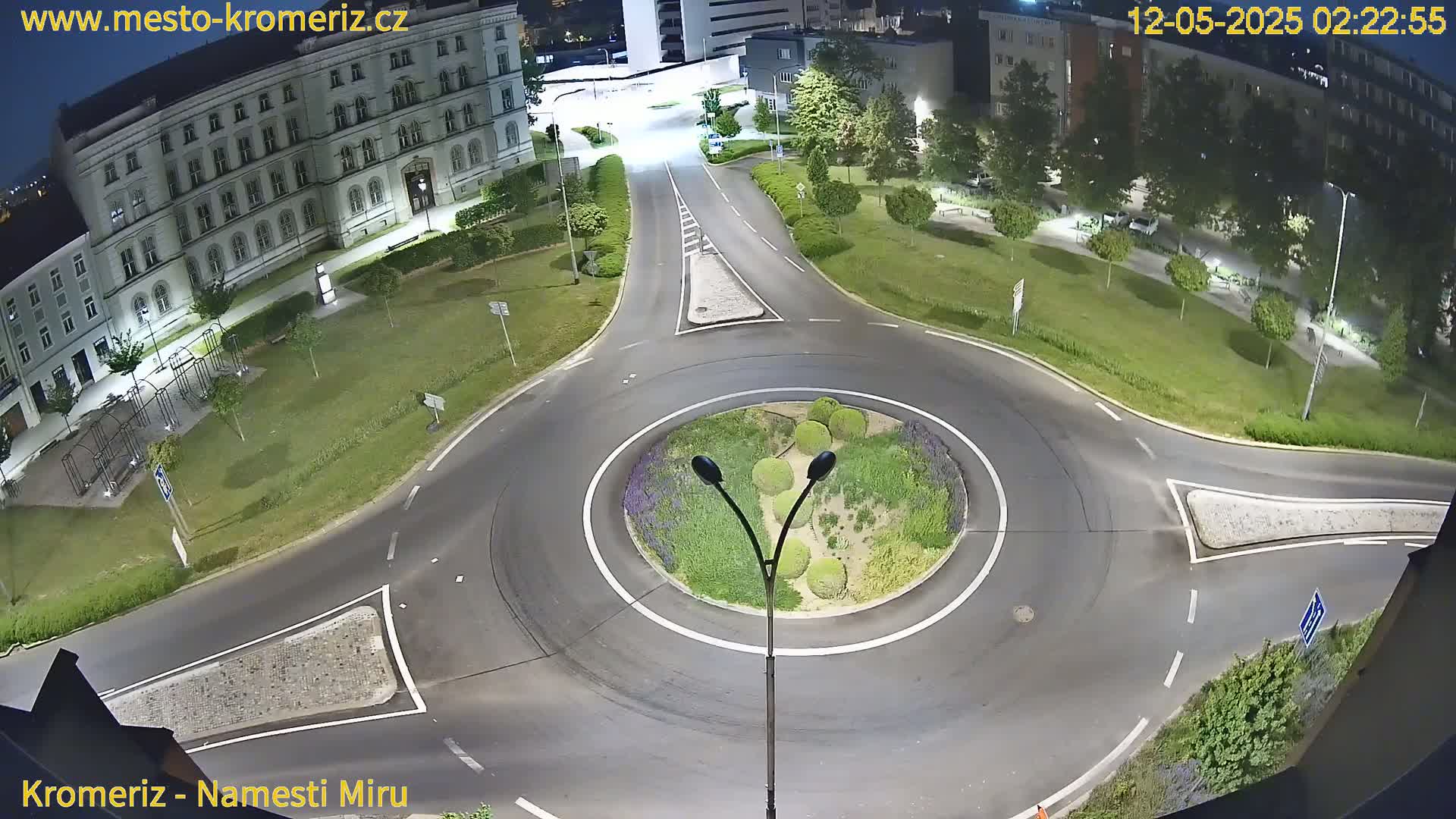 A nighttime aerial view of a roundabout surrounded by a grassy area, buildings, and streetlights.