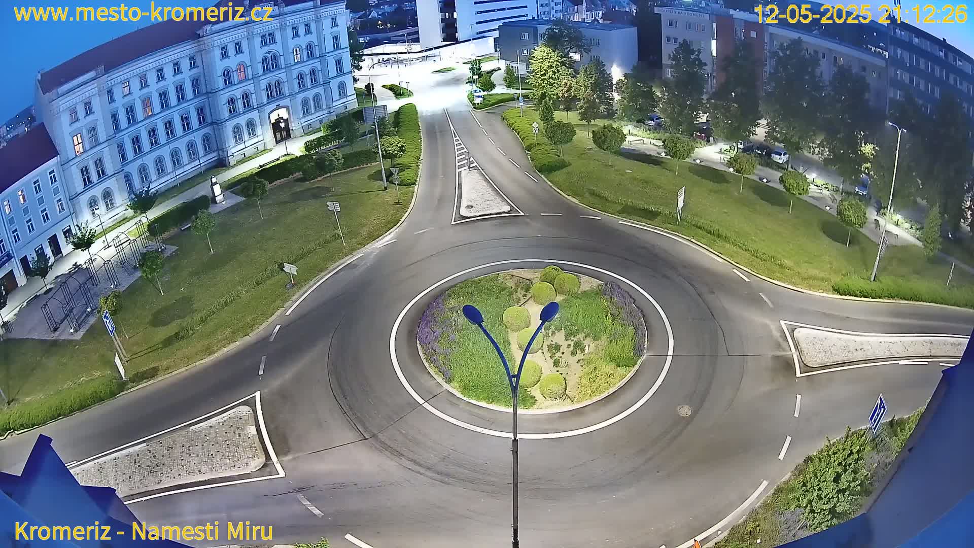 A nighttime aerial view shows a roundabout surrounded by roads, buildings, and landscaped areas.