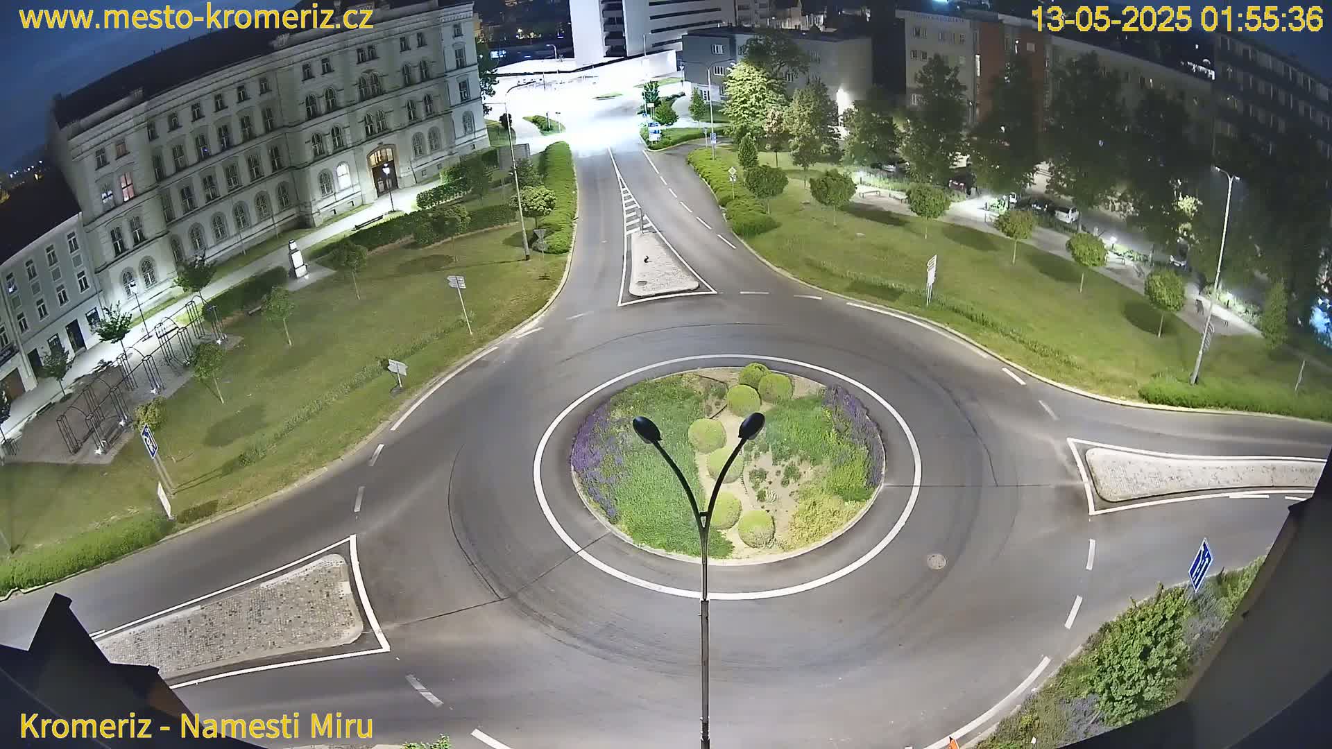 A nighttime overhead view of a roundabout surrounded by grassy areas, buildings, and streetlights.