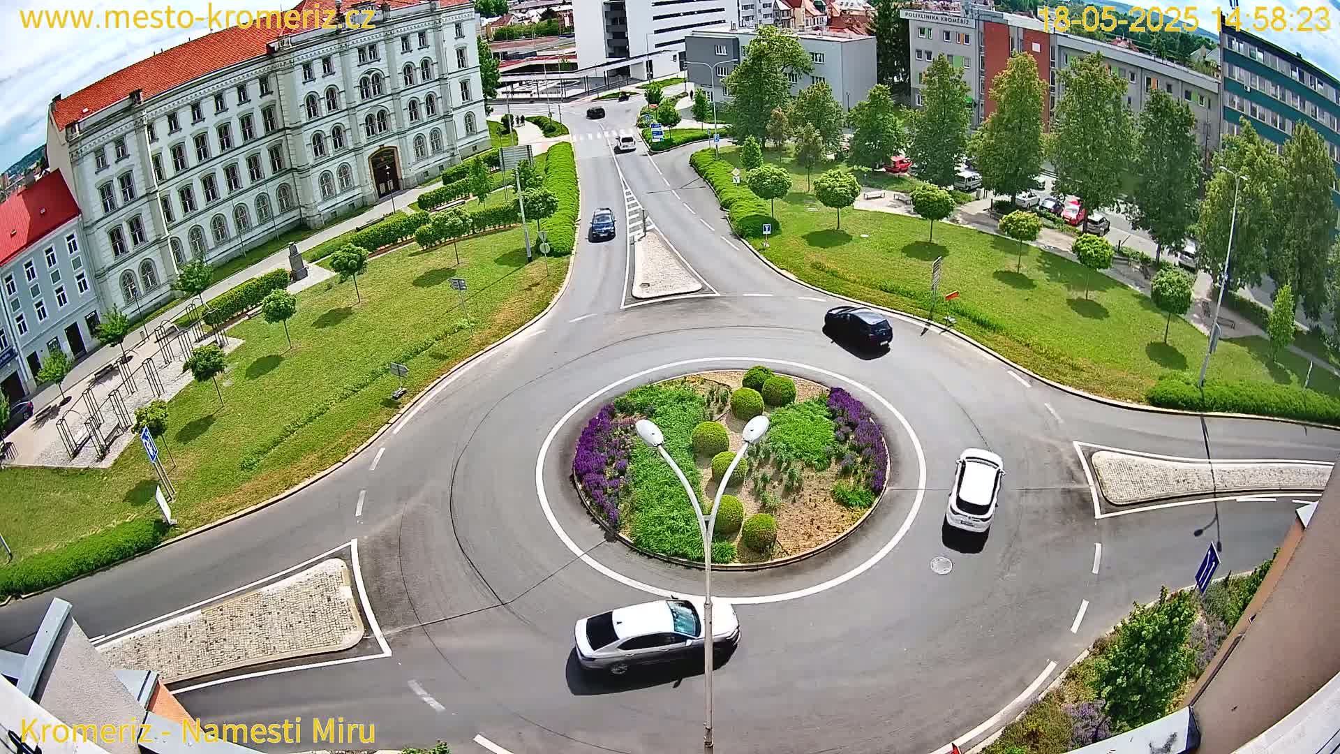 A roundabout with several cars and a large building visible in the background under a partly sunny sky.