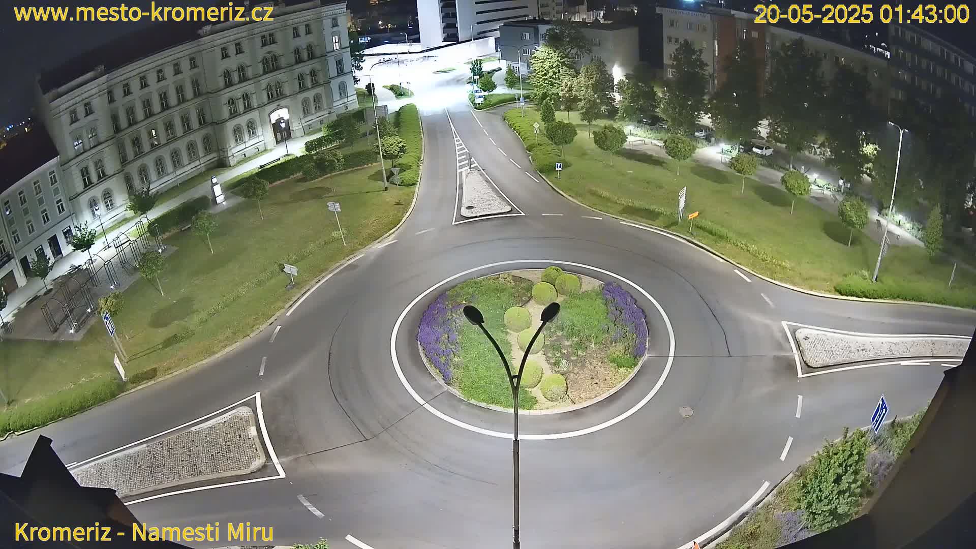 A nighttime overhead view of a roundabout surrounded by a grassy area, buildings, and streetlights.