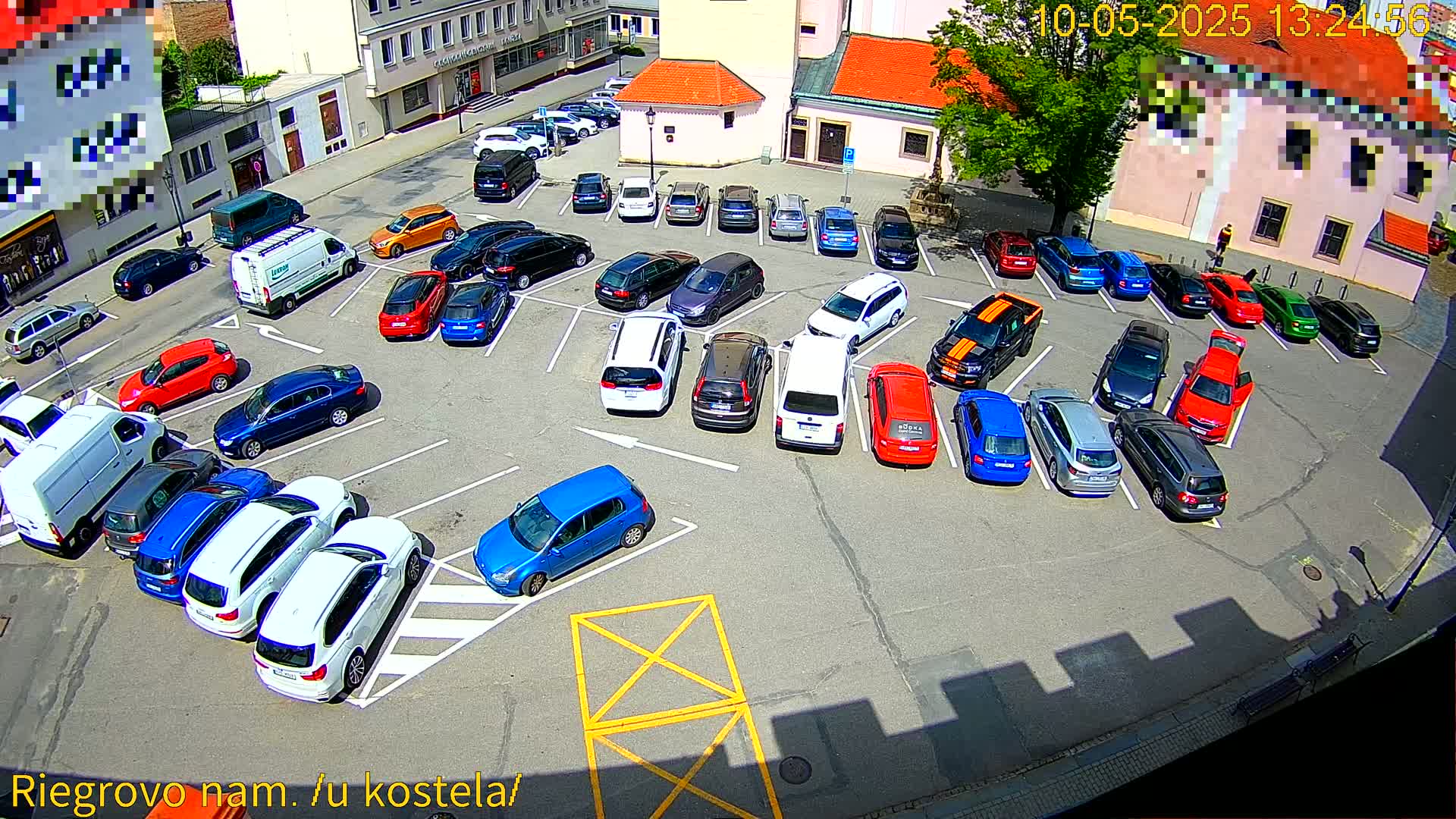 A sunny day shows a parking lot filled with a variety of cars, mostly parked in rows.