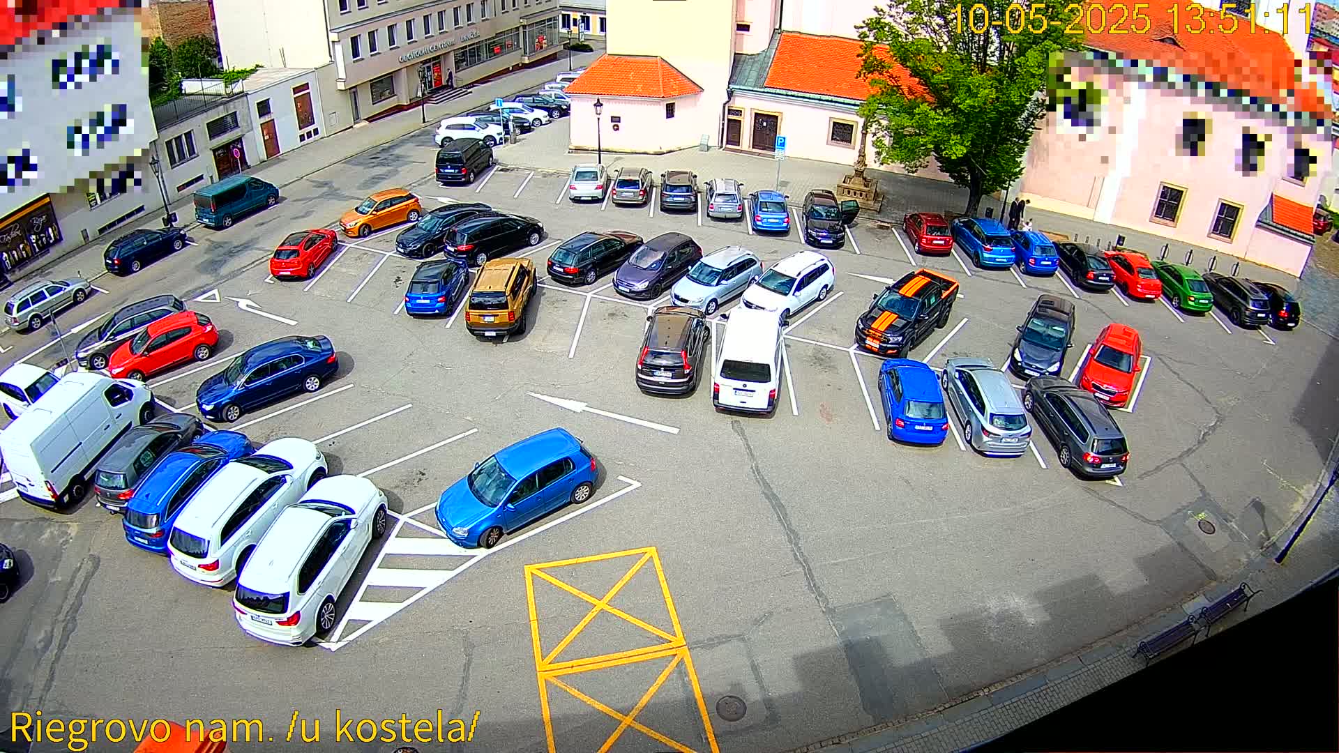 A full parking lot of various colored cars is viewed from above on a sunny day.