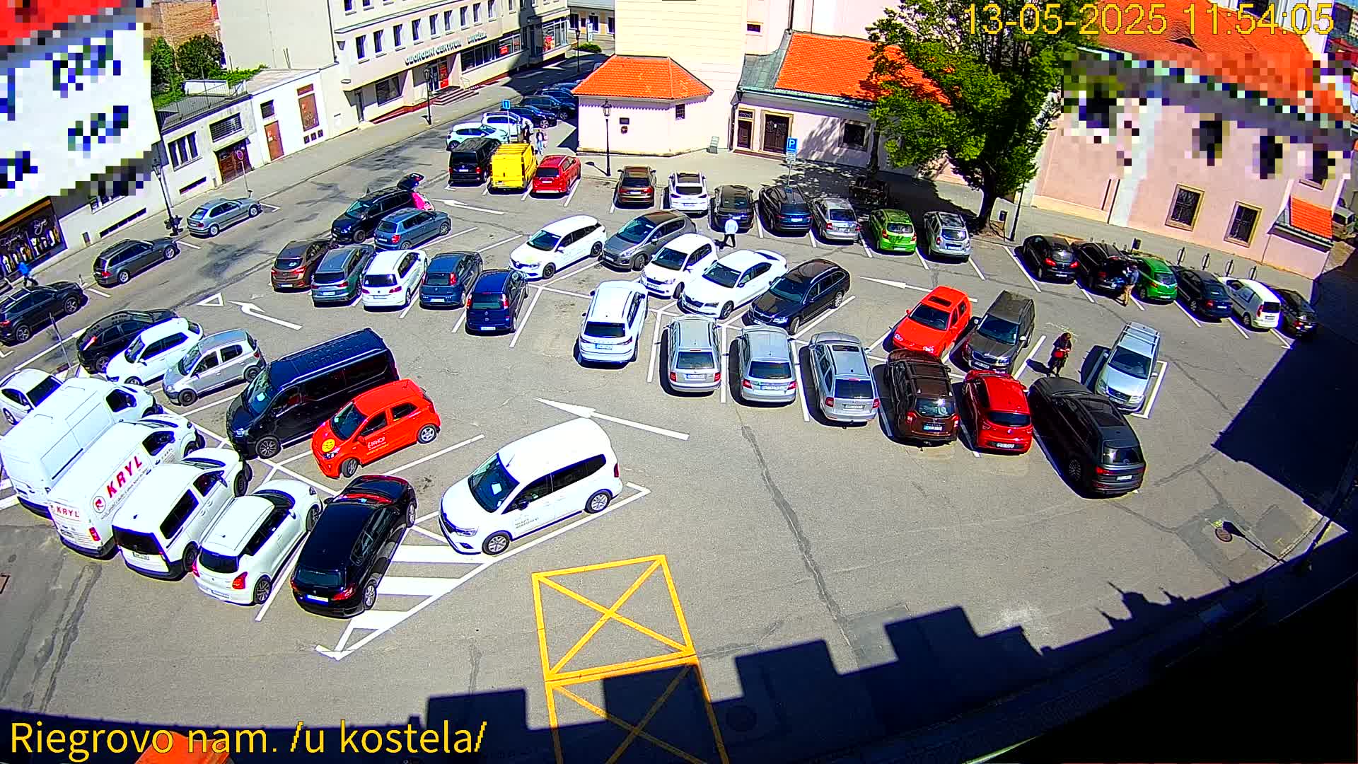 A sunny day reveals a full parking lot with numerous cars of various makes and colors parked in a paved area near buildings.