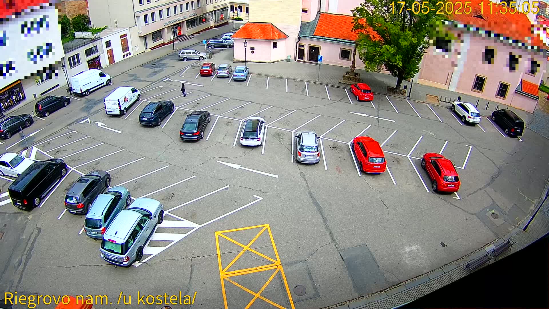 A mostly full parking lot with numerous cars parked in marked spaces,  surrounded by buildings on a sunny day.