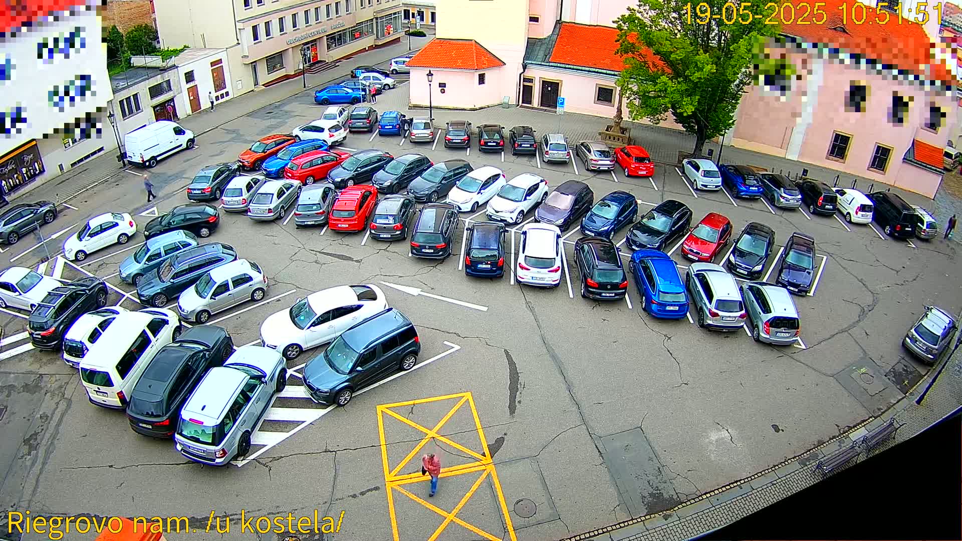 A mostly full parking lot with numerous cars of various colors and models, situated outdoors on a mostly overcast day, with one person walking across the lot.