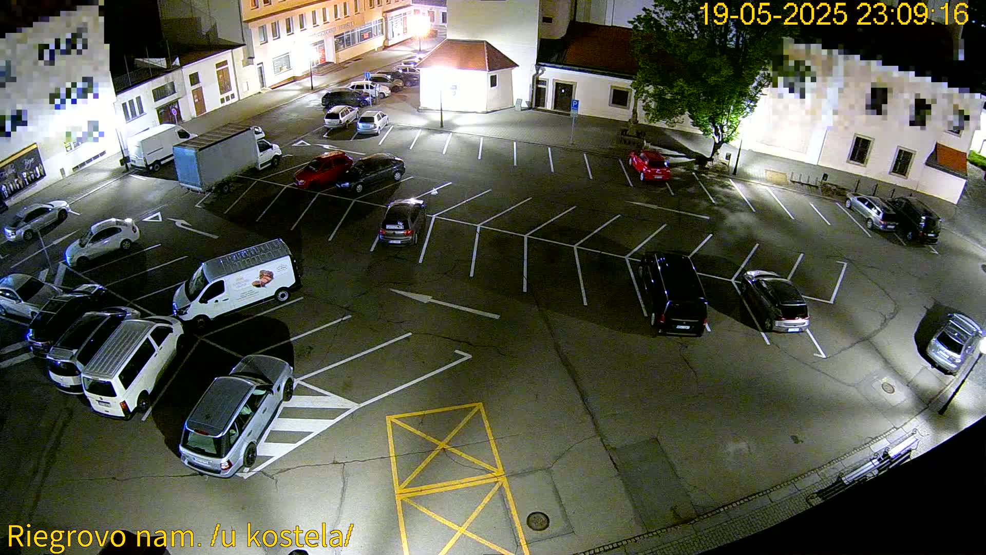 An empty parking lot at night, illuminated by streetlights, is filled with numerous parked cars under a clear sky.