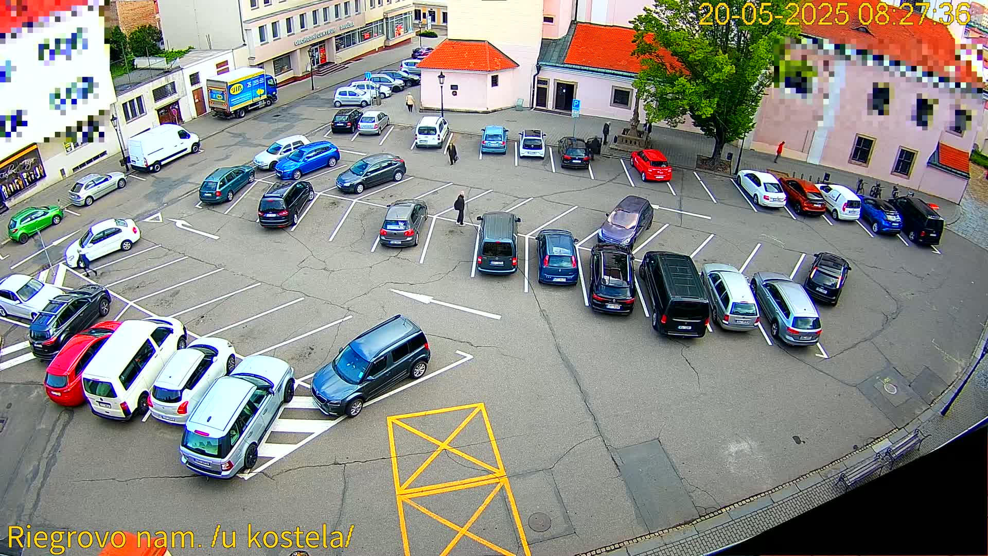 An asphalt parking lot filled with various cars, surrounded by buildings, under a partly cloudy sky.