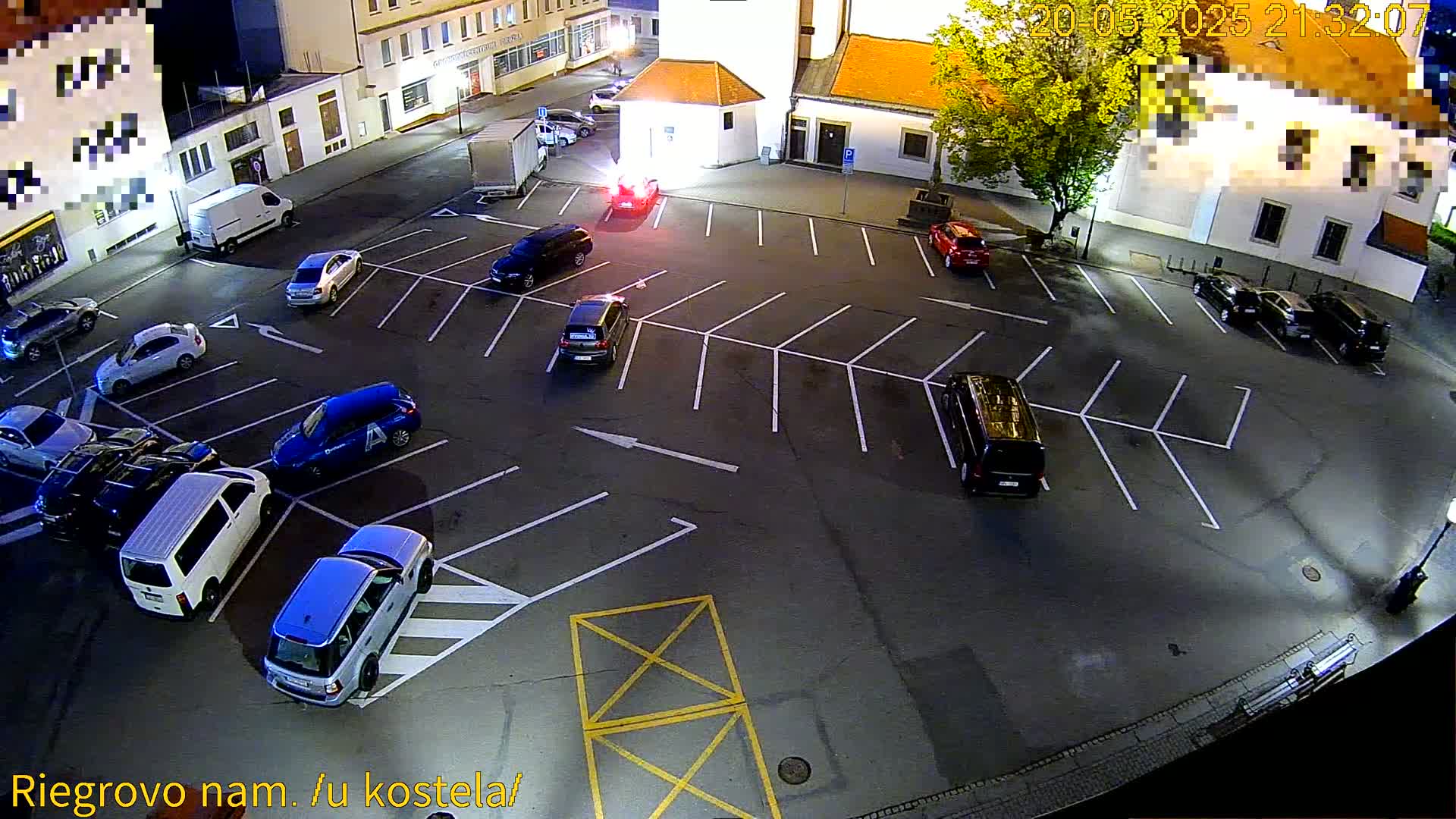 A nighttime aerial view shows a mostly empty parking lot with several cars parked, under artificial lighting.