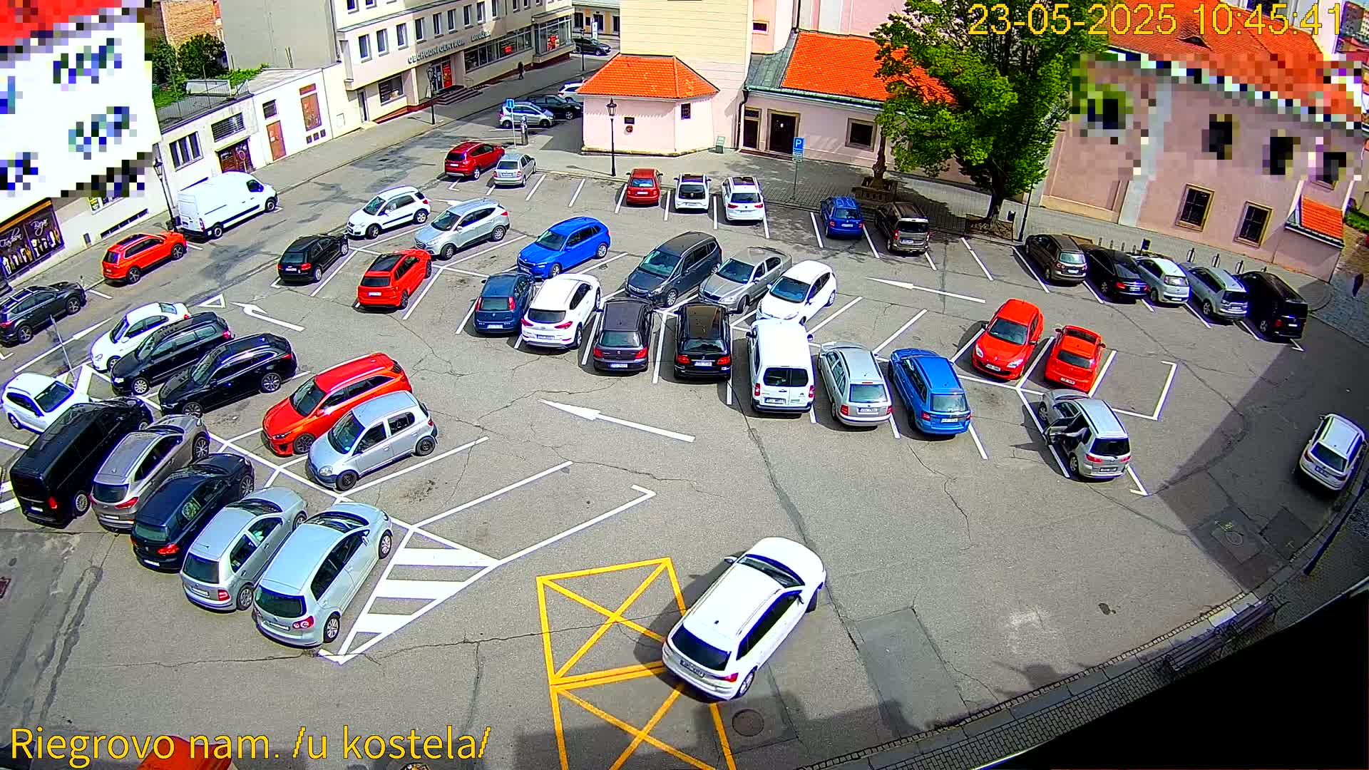 A full parking lot of various cars is viewed from above on a sunny day.