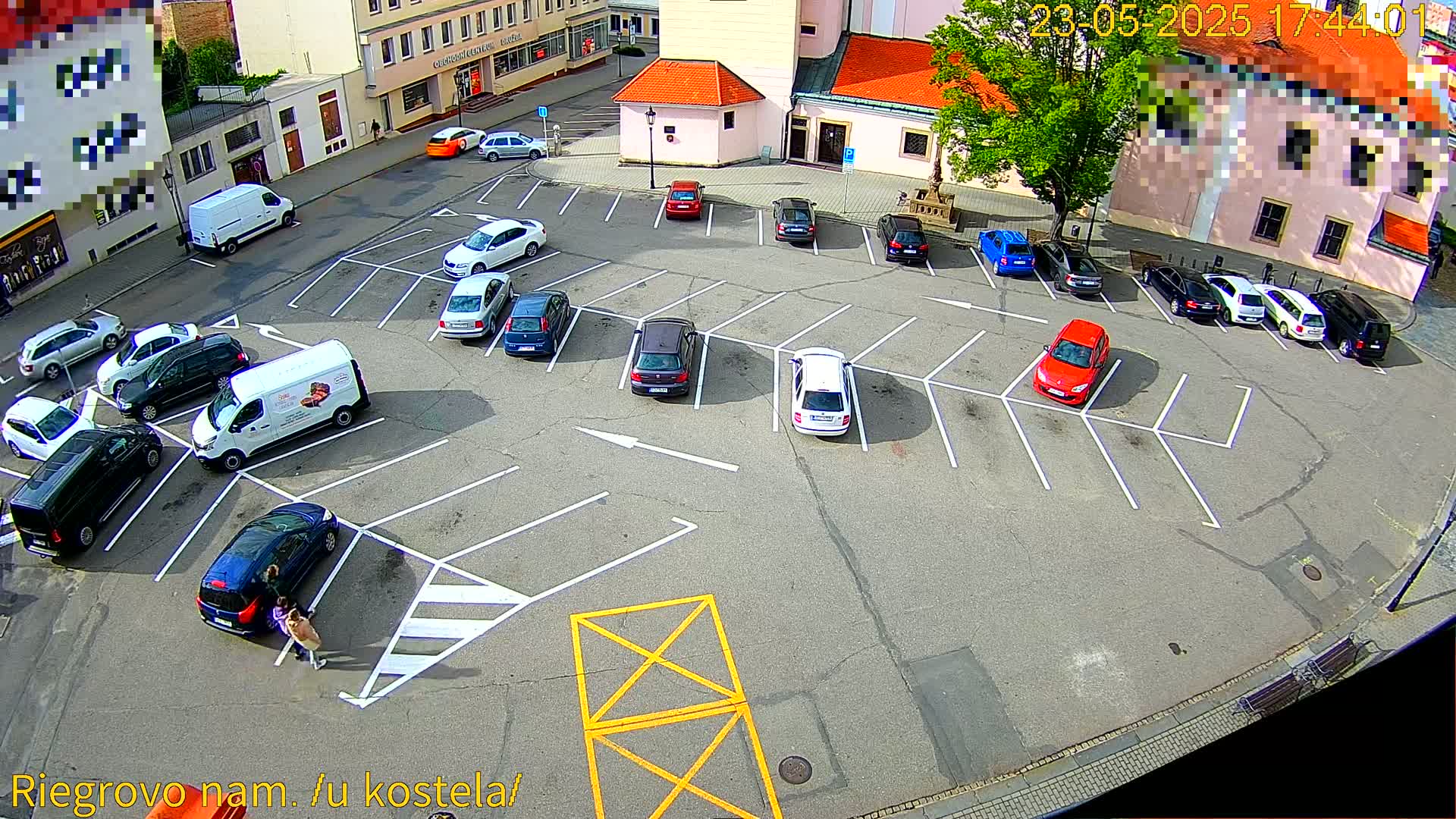 A mostly empty parking lot with numerous cars parked in marked spaces, under a sunny sky.
