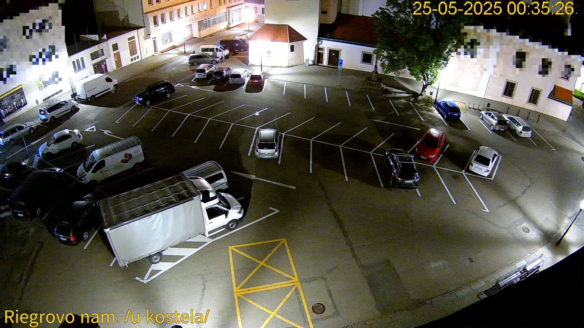A mostly empty parking lot at night is filled with several cars and vans, illuminated by streetlights.