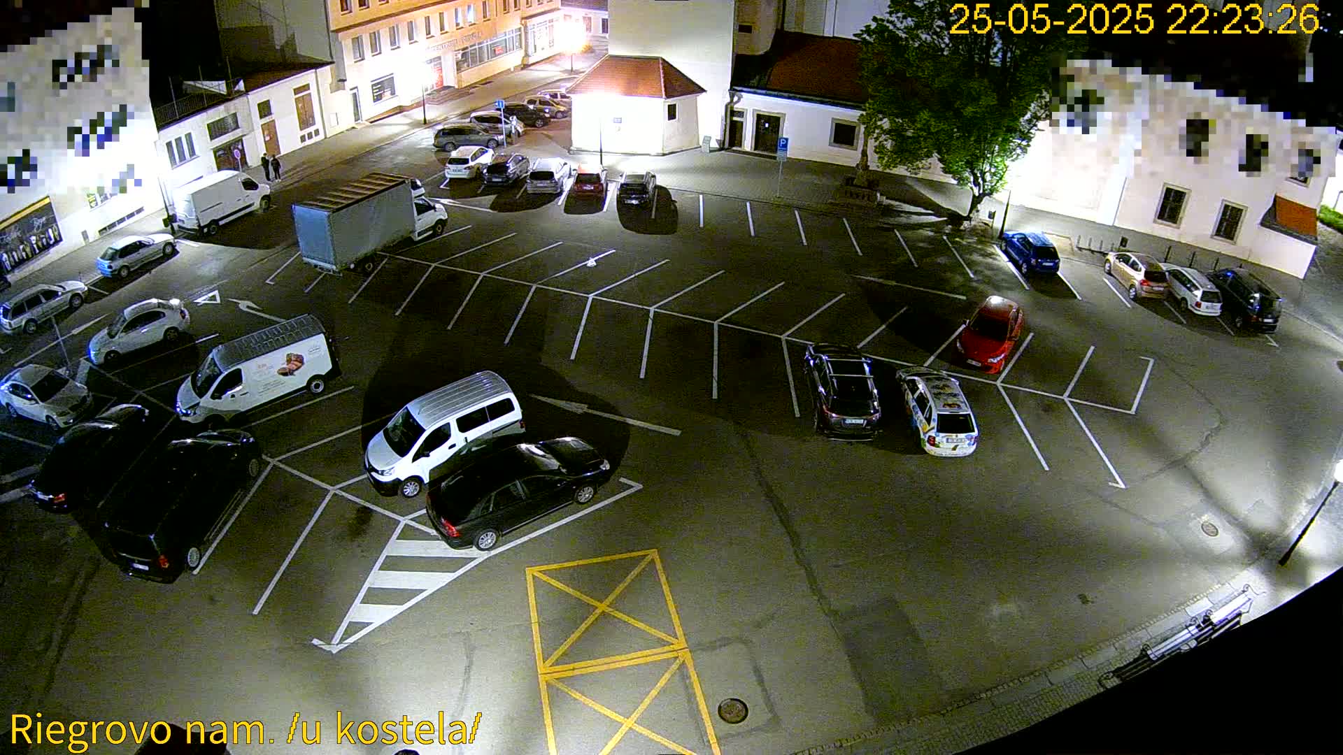 A nighttime aerial view of a mostly empty parking lot with several cars and vans parked, under clear skies.