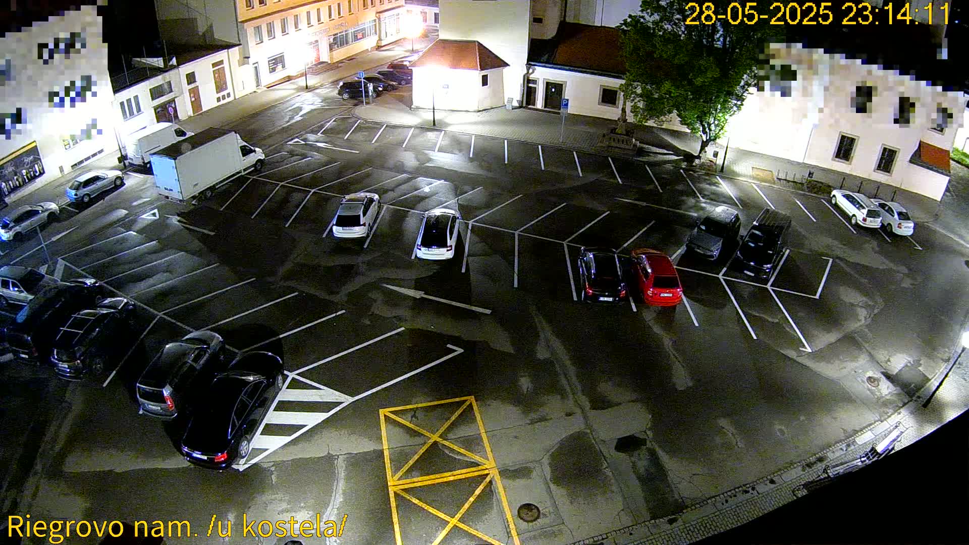 A wet, nighttime parking lot with several cars parked, and a truck nearby, is illuminated by streetlights.
