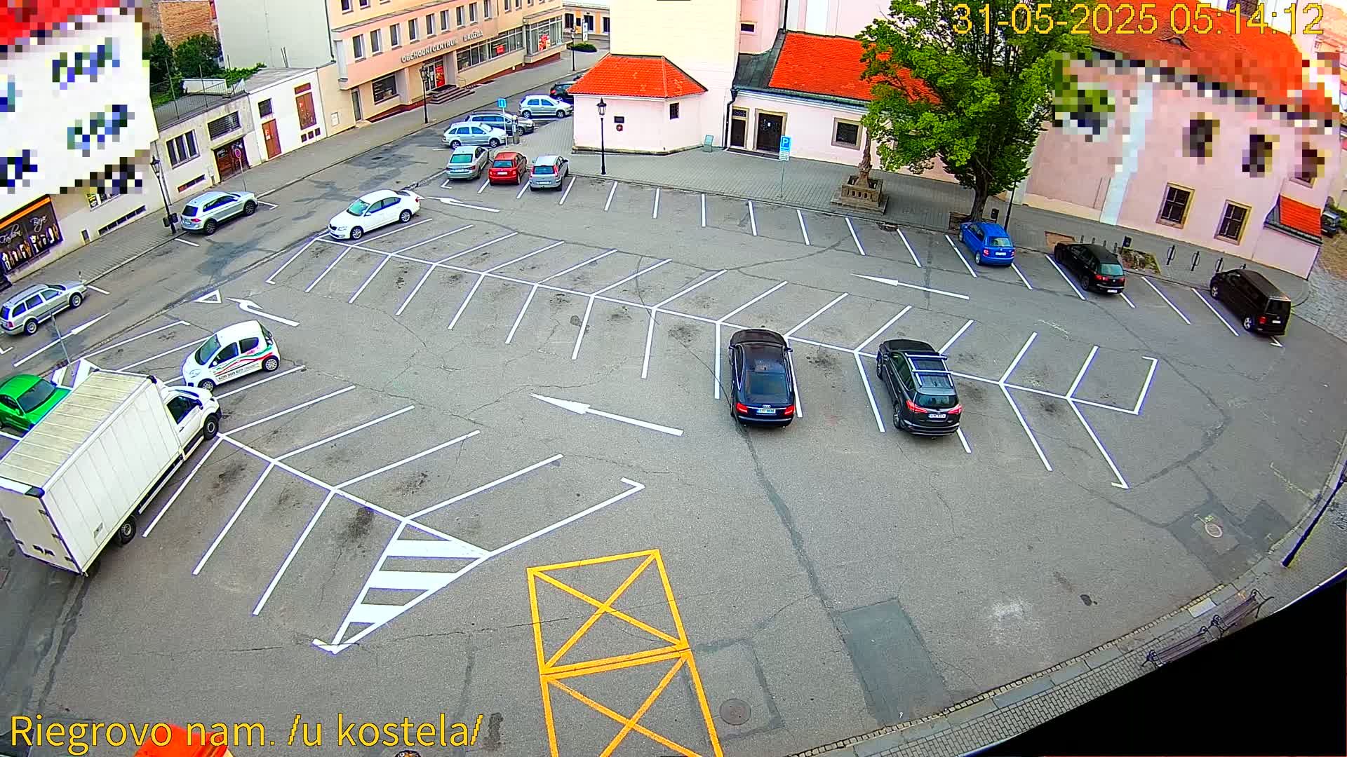 An asphalt parking lot with numerous cars parked, situated next to buildings under a partly sunny sky.