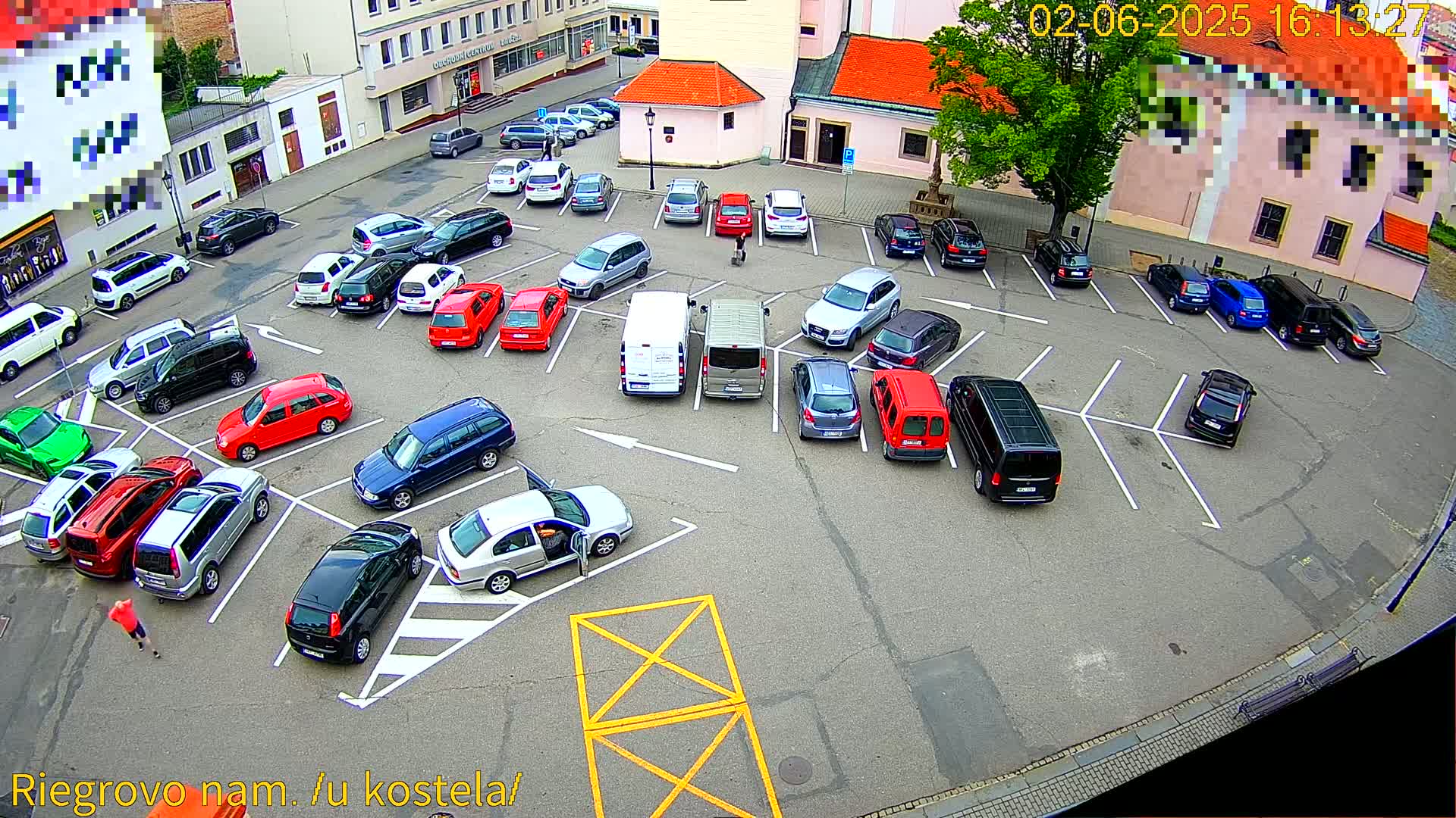 A mostly full parking lot with various cars, vans, and an SUV is viewed from above on a partly sunny day.