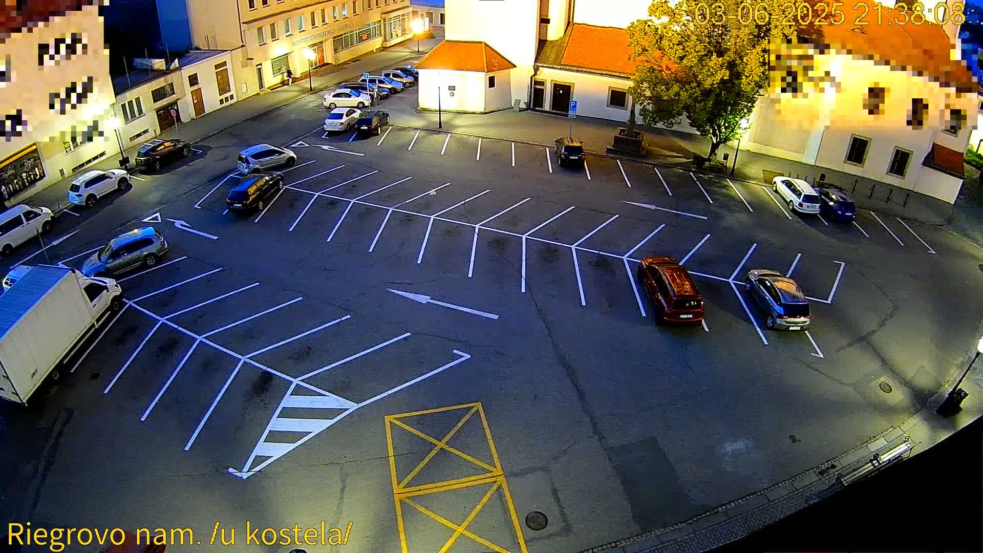 An empty parking lot at night with several cars parked in it, near some buildings.