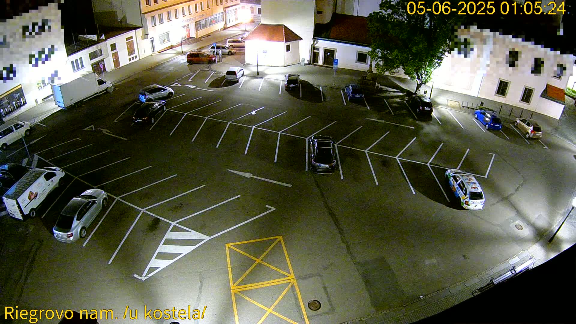 An empty asphalt parking lot at night, illuminated by artificial lights, is filled with several parked cars and vans.