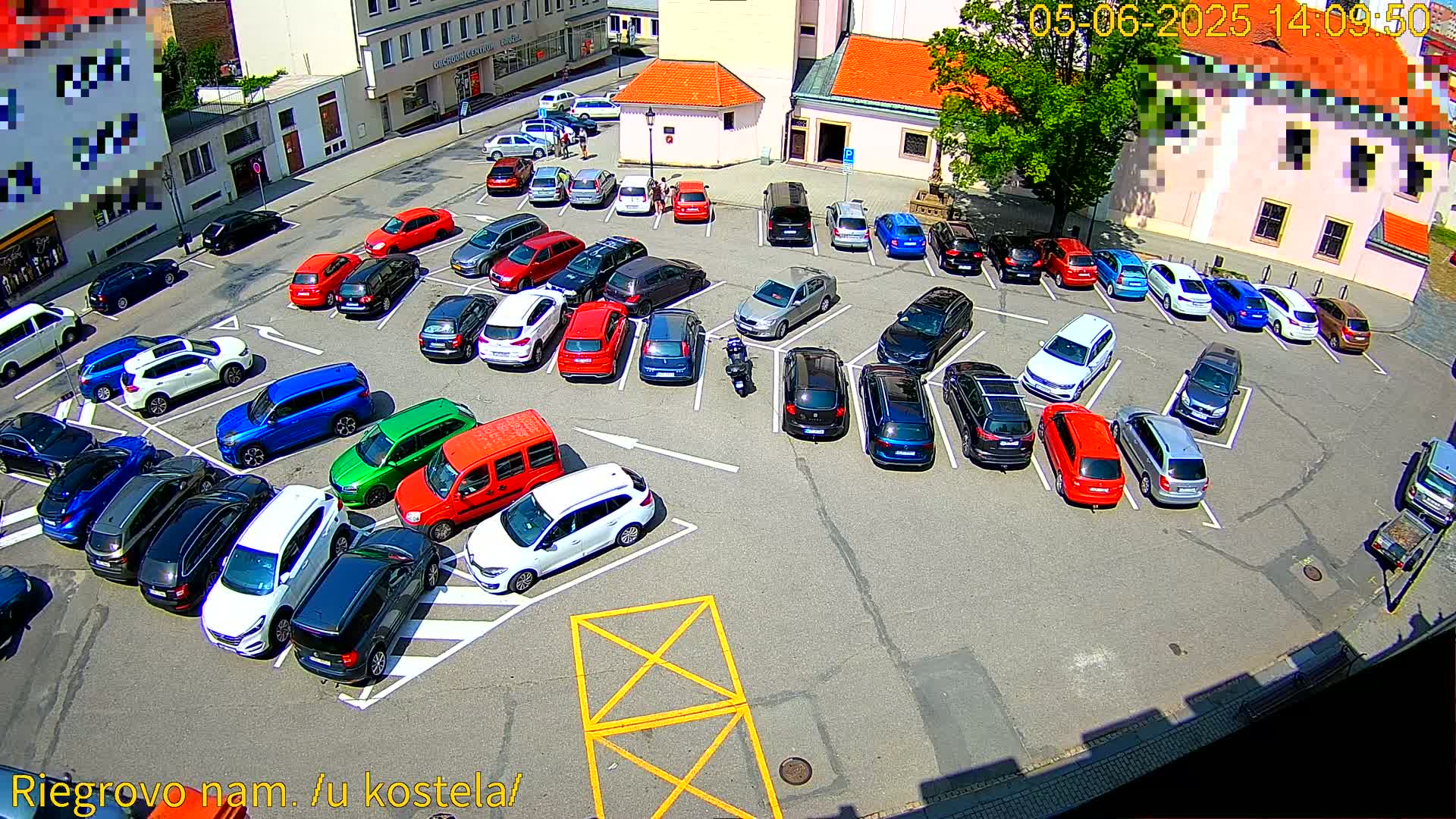 A mostly full parking lot with a variety of colored cars, under sunny conditions, is viewed from above.