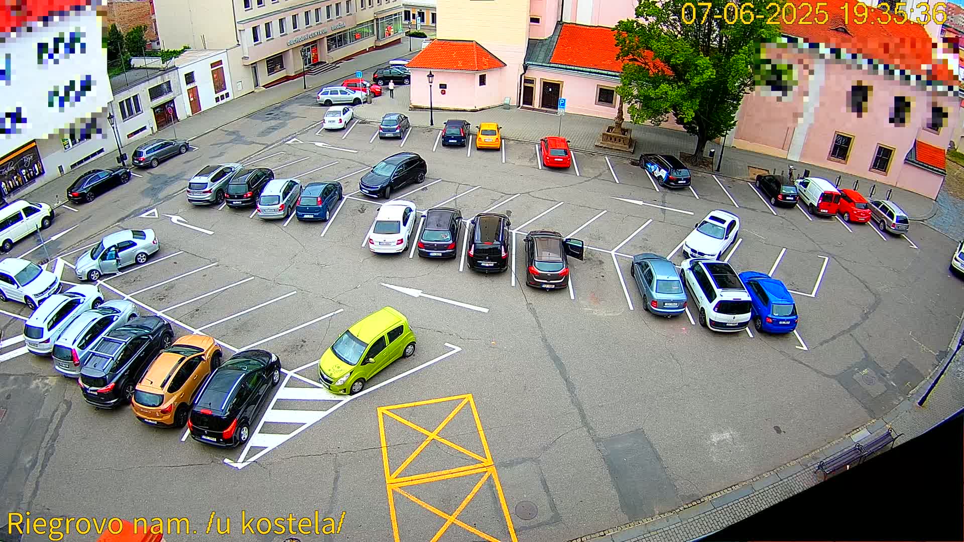 A mostly full parking lot with a variety of cars is viewed from above on a partly sunny day.