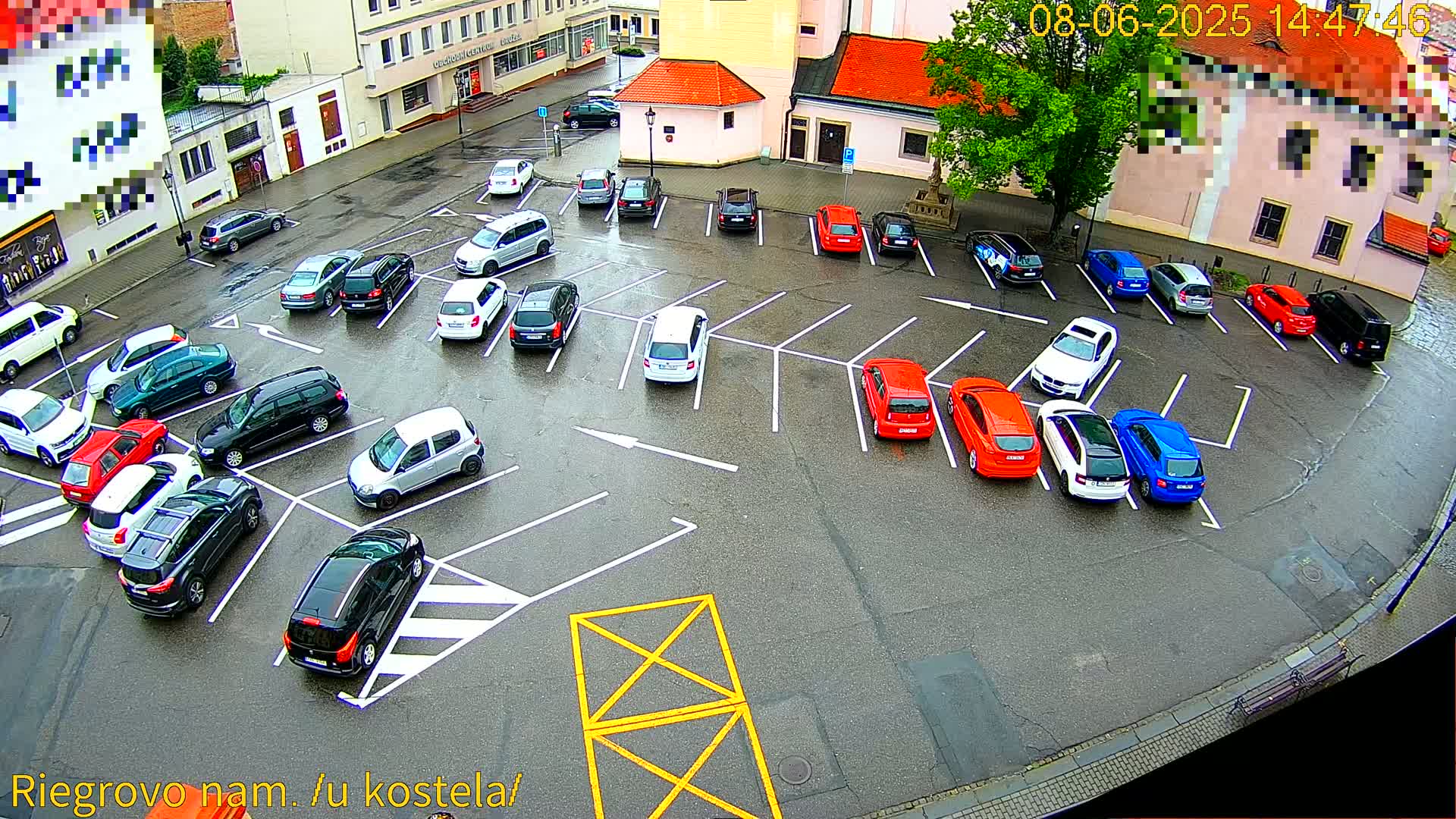 A wet parking lot is filled with numerous cars parked in designated spaces.