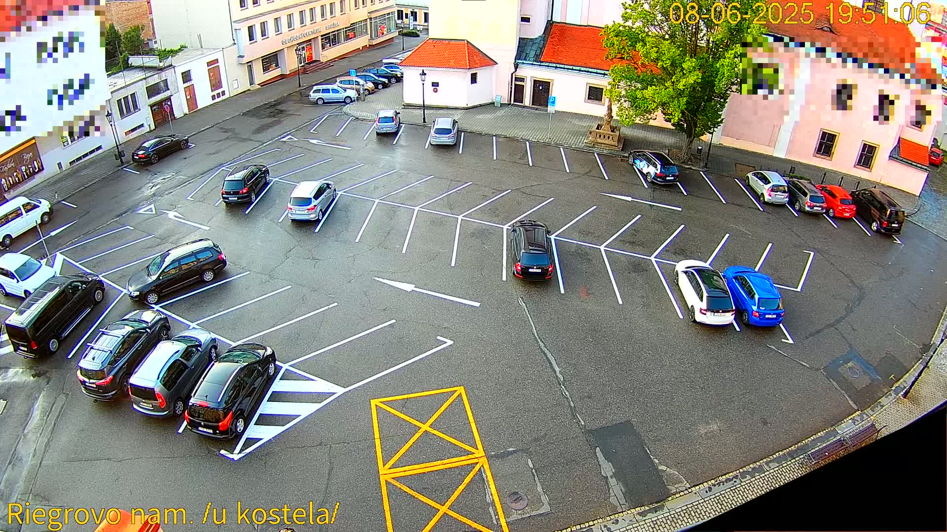 An asphalt parking lot with numerous cars parked in marked spaces, surrounded by buildings under a clear evening sky.