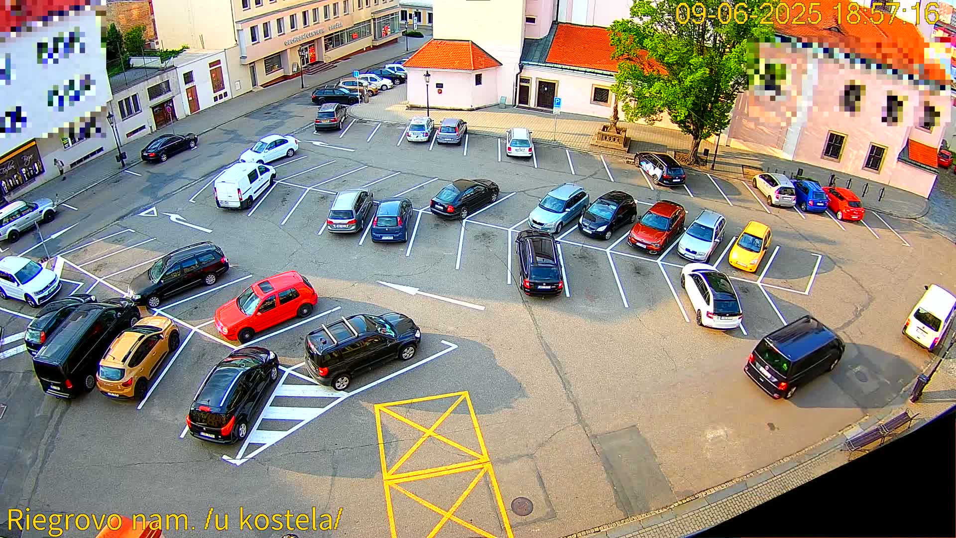 An overhead view of a mostly full parking lot in a town square on a sunny day.