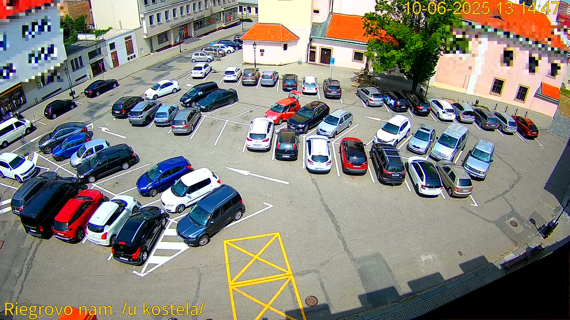 A full parking lot viewed from above on a sunny day is filled with various cars and small SUVs.