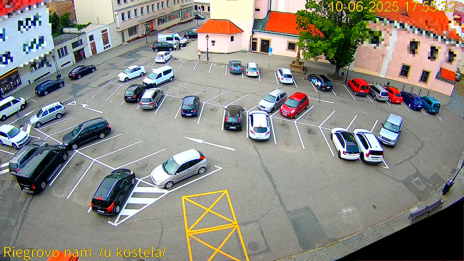 A mostly full parking lot with various cars parked in spaces, viewed from above on a clear day.