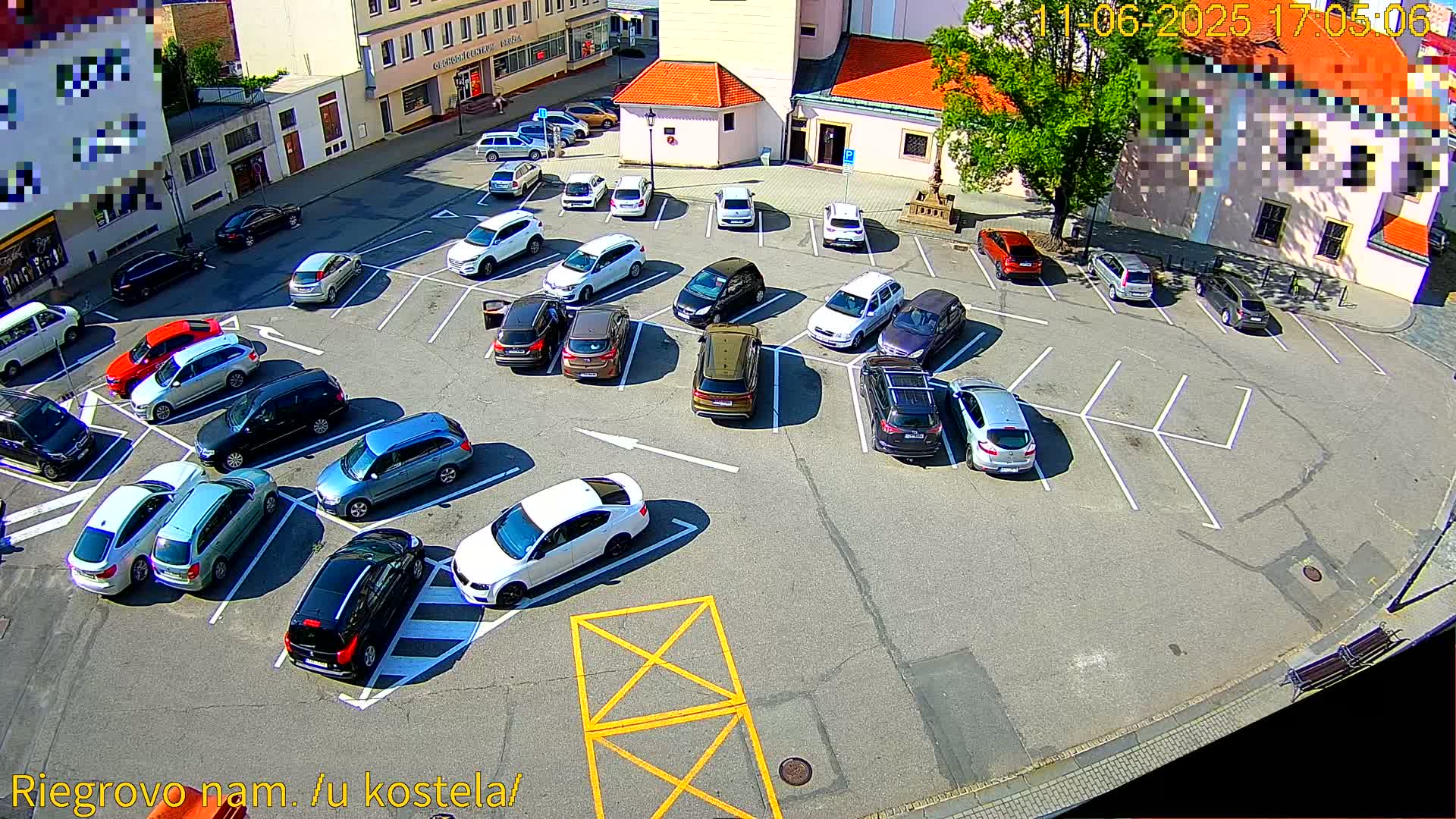 A sunny day shows a full parking lot of various cars surrounding a town square.