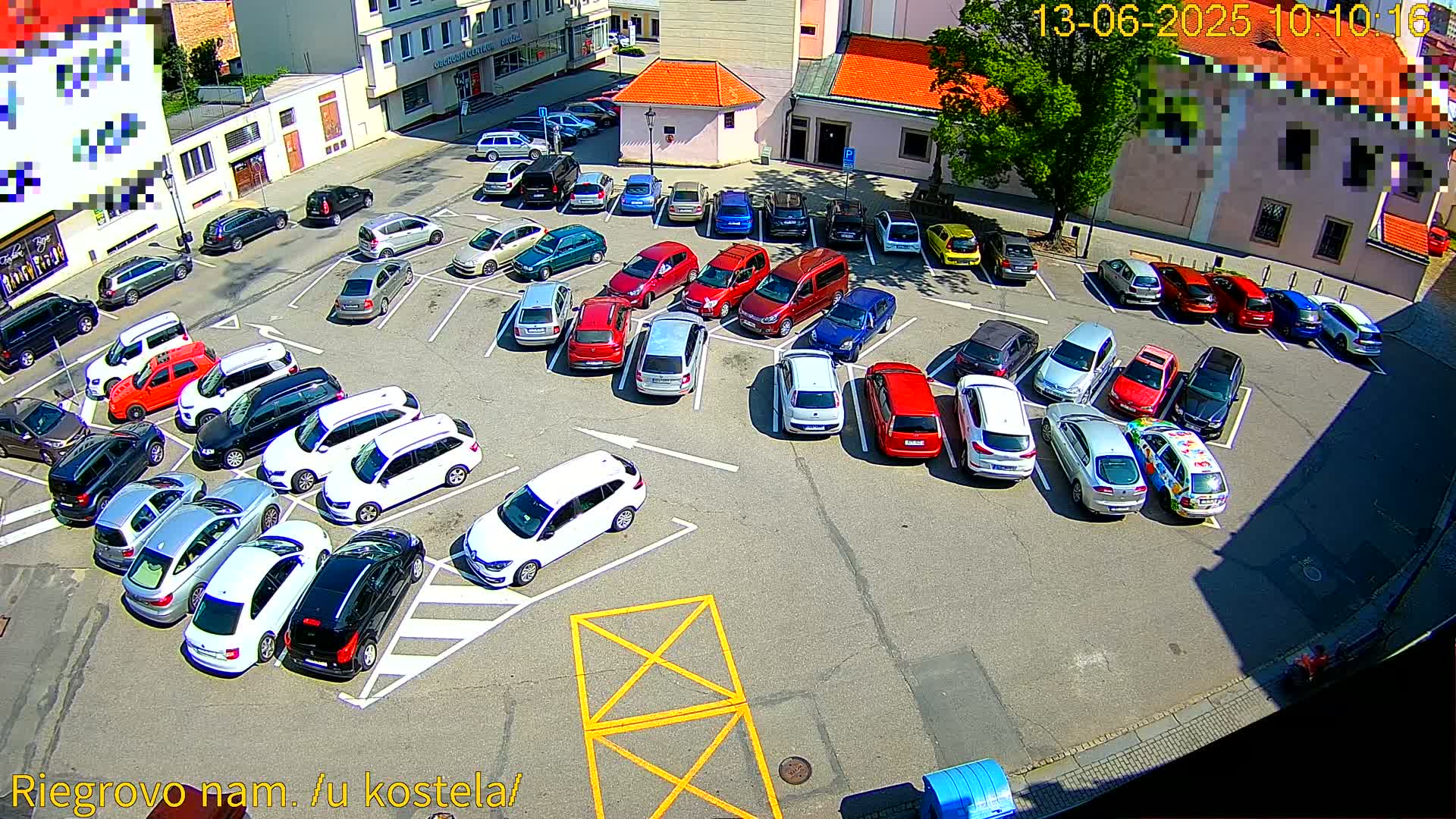 A sunny day reveals a full parking lot with numerous cars parked in rows, many of which are white, silver, or red.