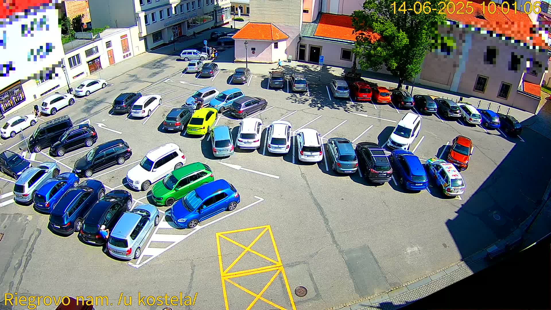 A sunny day reveals a parking lot filled with numerous cars of various colors and models, parked in designated spaces.