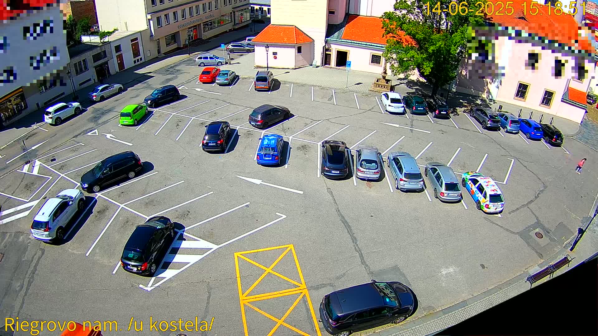 A sunny day aerial view of a mostly full parking lot surrounded by buildings.