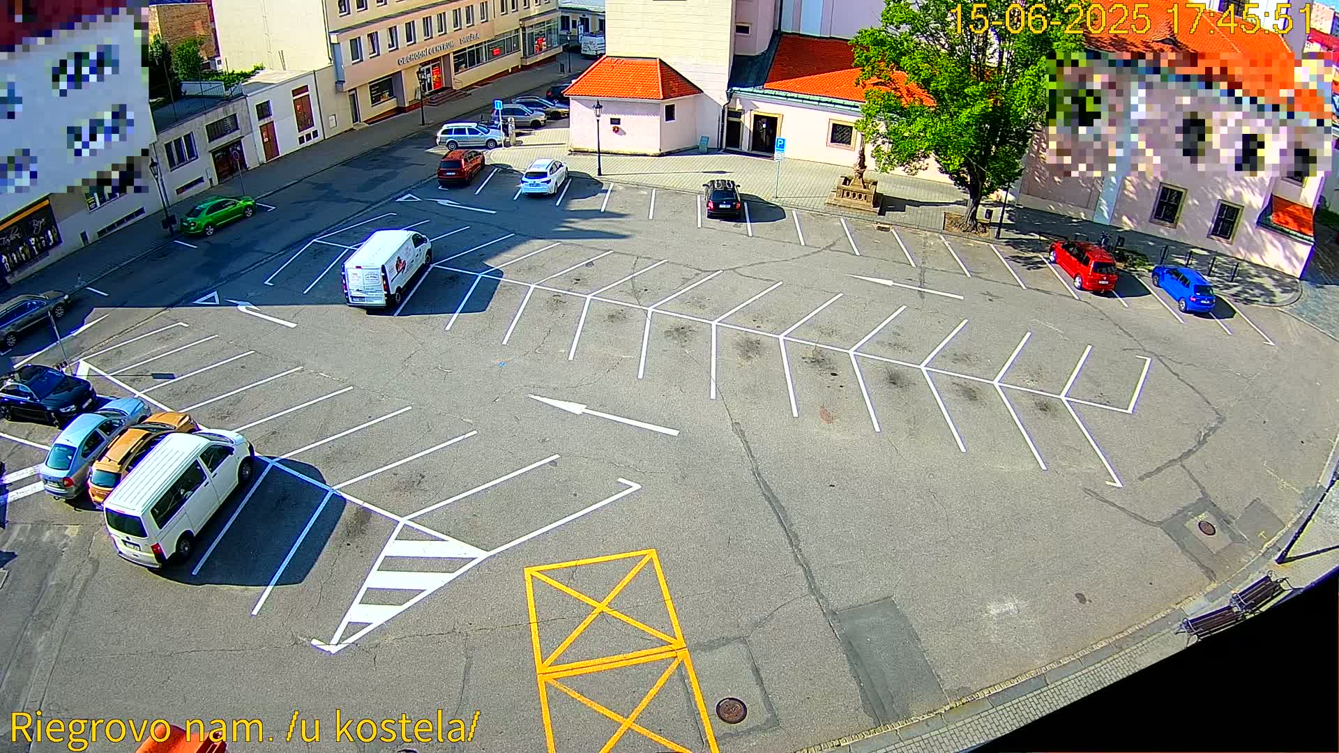 A mostly empty parking lot with several cars parked, situated in front of buildings on a sunny day.