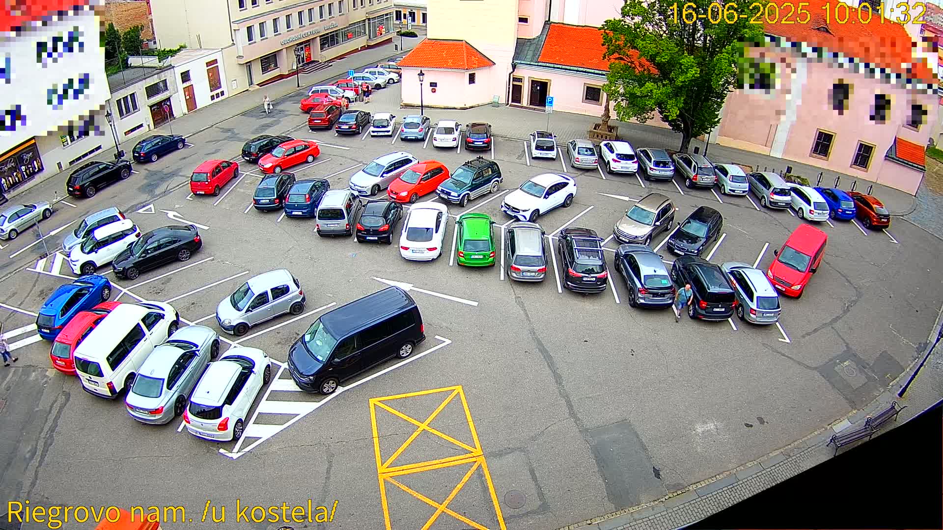 A mostly full parking lot with a variety of cars parked in a paved area, viewed from above on a partly cloudy day.