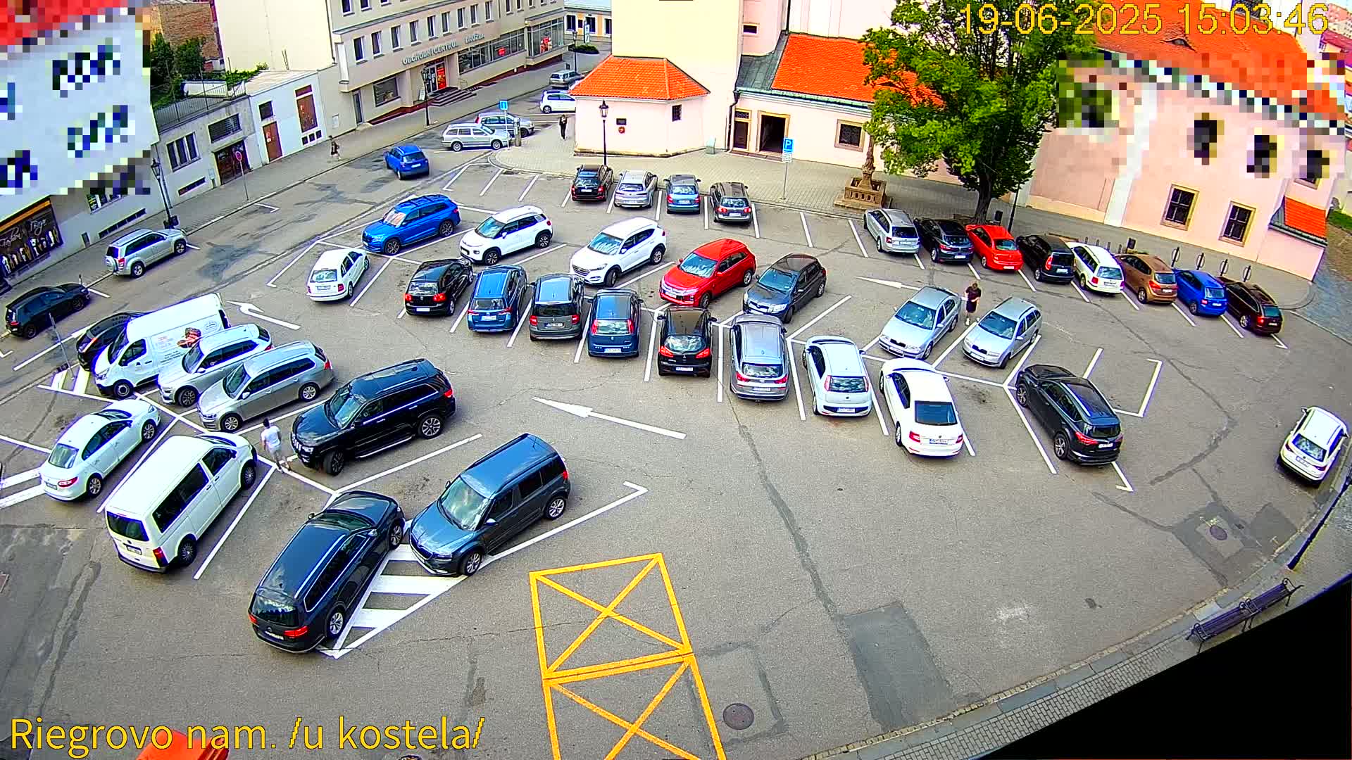 A full parking lot of various cars is viewed from above on a sunny day.