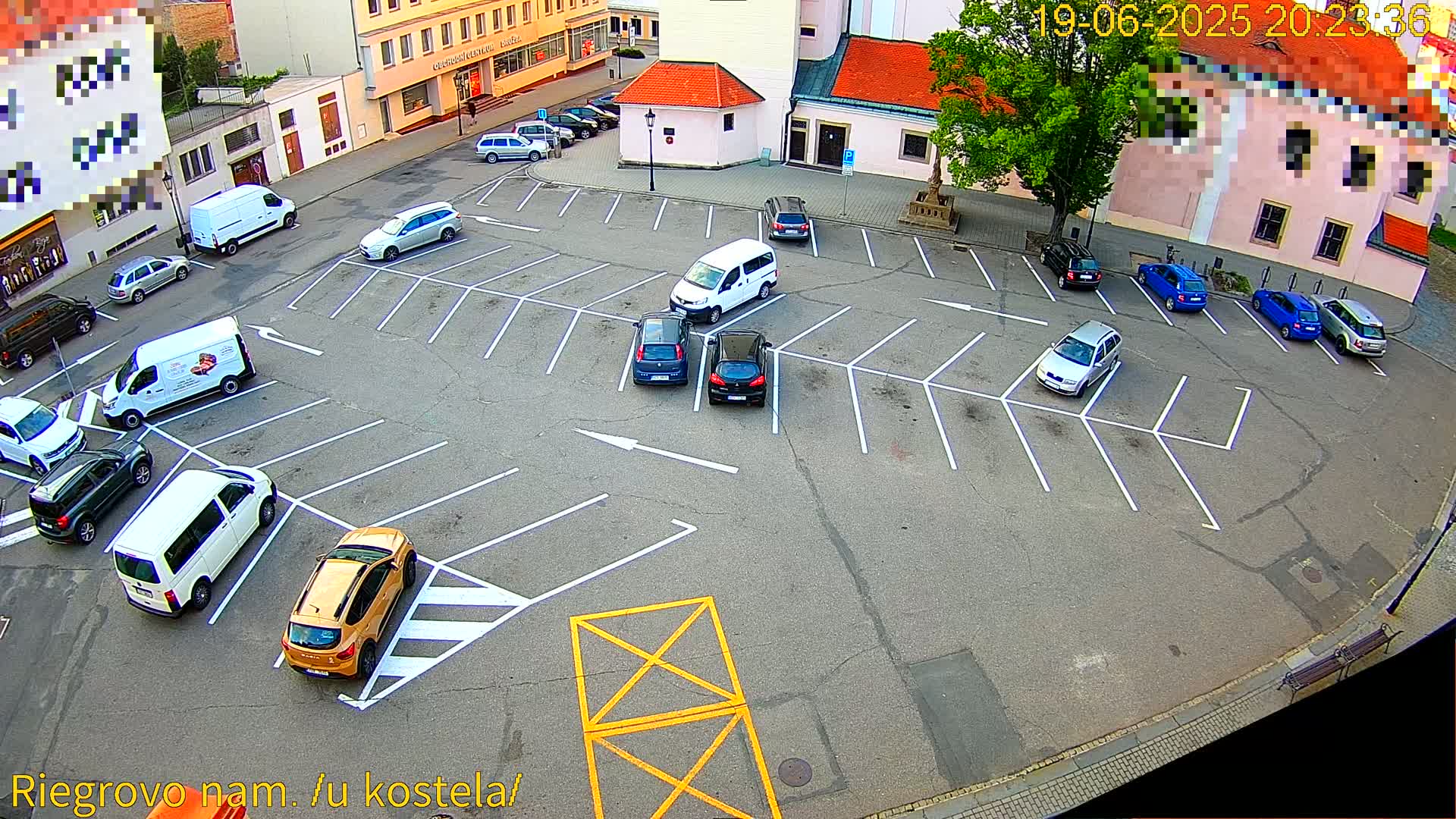 An asphalt parking lot with numerous cars and vans parked in marked spaces, surrounded by buildings under a clear sky.