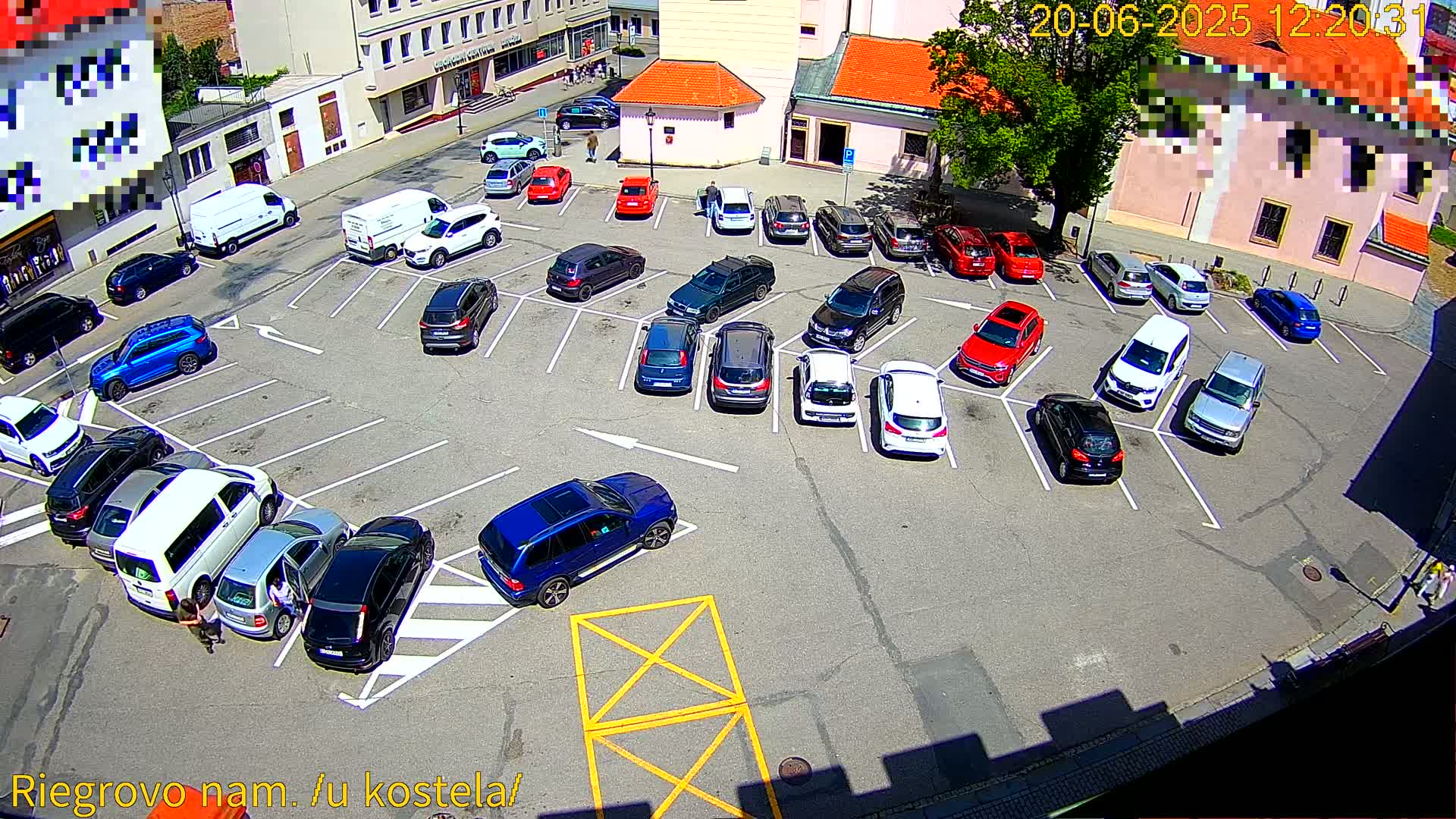 A sunny day shows a parking lot full of cars, with several people walking nearby.