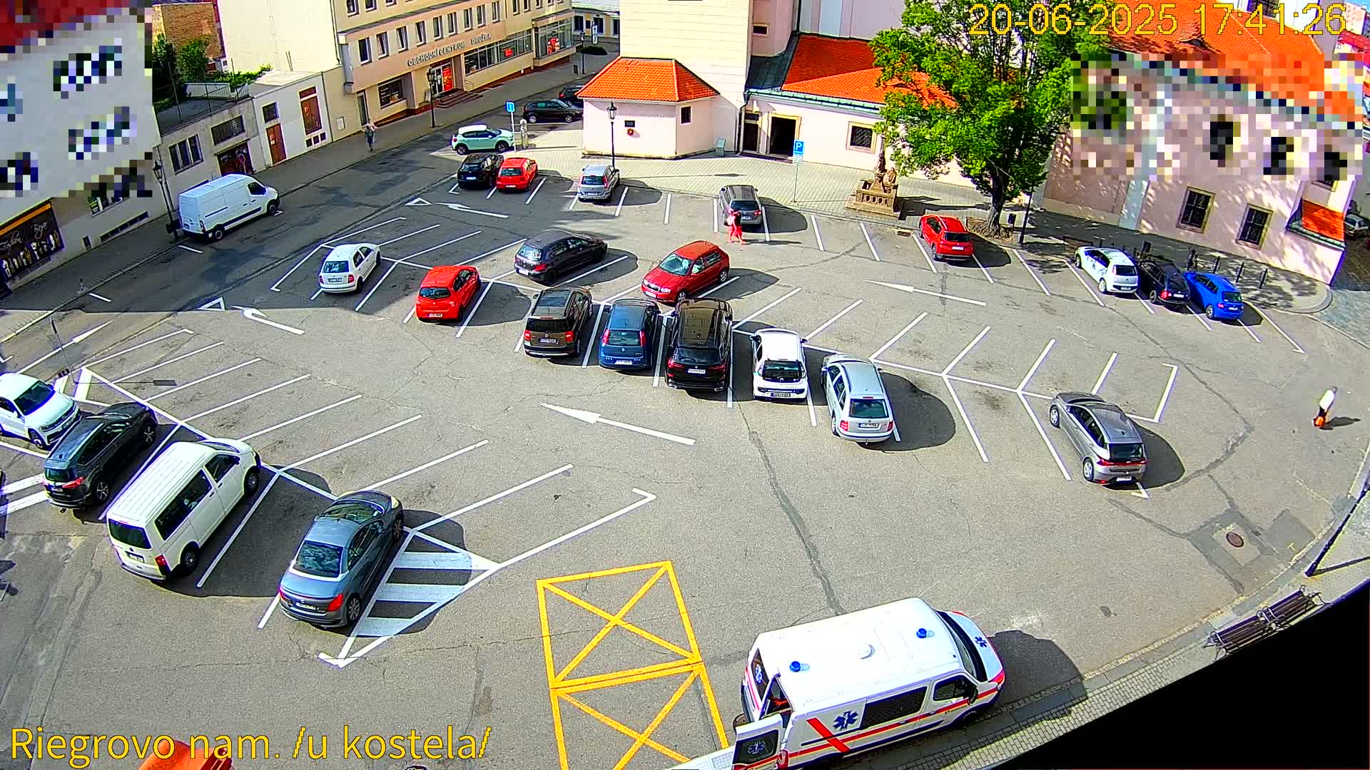 An aerial view of a mostly empty parking lot on a sunny day, with numerous cars parked in designated spaces, and an ambulance at the bottom.