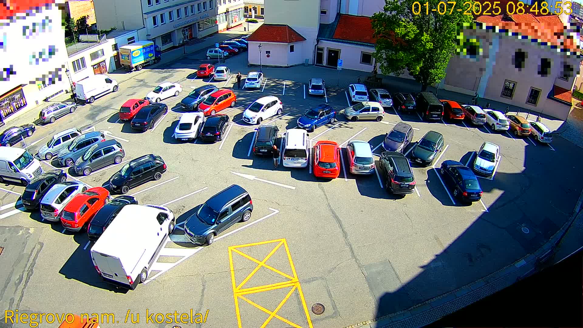 A sunny day reveals a full parking lot with numerous cars parked in spaces, surrounded by buildings.